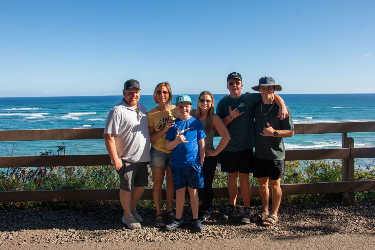 Group poses together at scenic coastal viewpoint with ocean waves and blue sky in background.