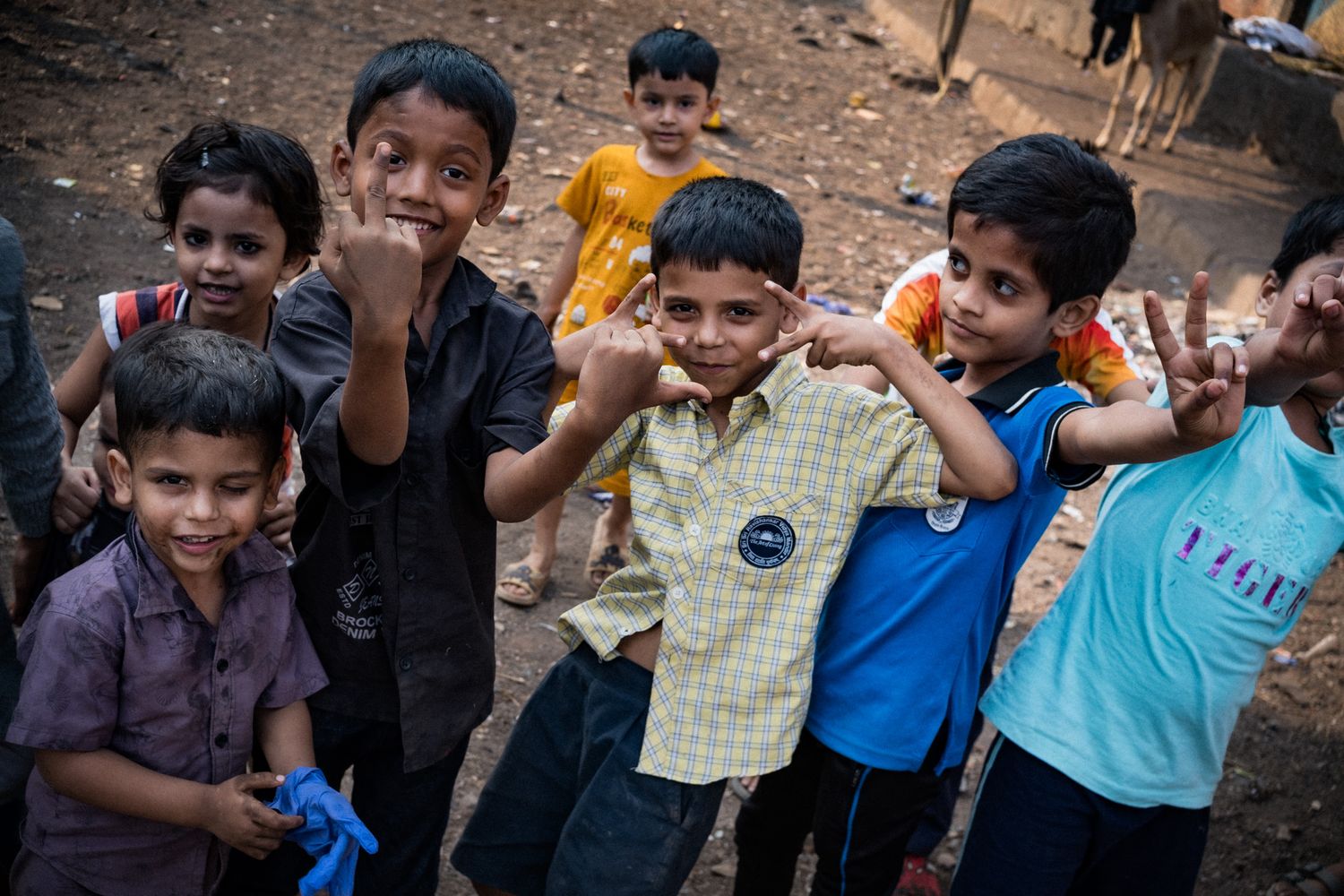 A group of cheerful Indian children posing and flexing muscles outdoors in a dusty playground area.