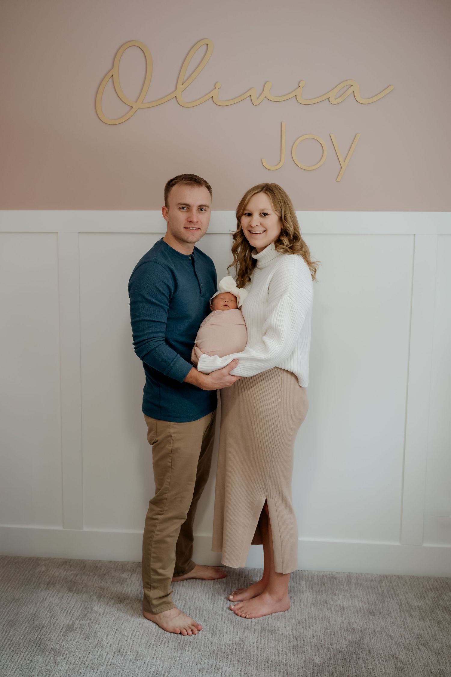 A couple in casual attire dances barefoot together on a gray carpet in front of a white wall.