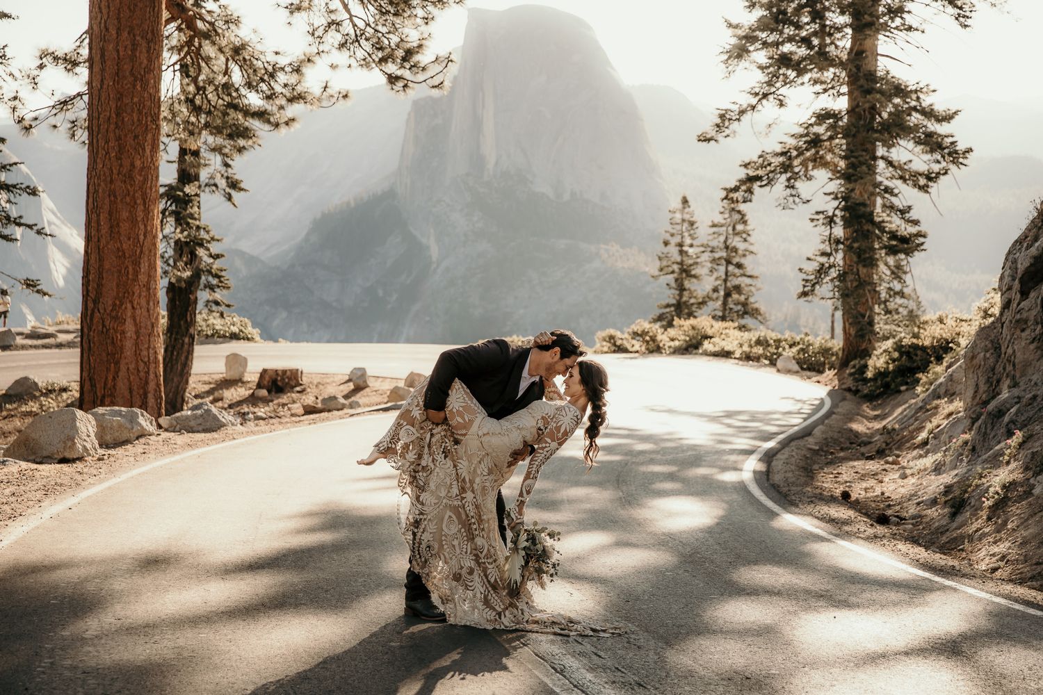 A couple embraces on a scenic mountain cliff overlooking a misty lake during golden hour.