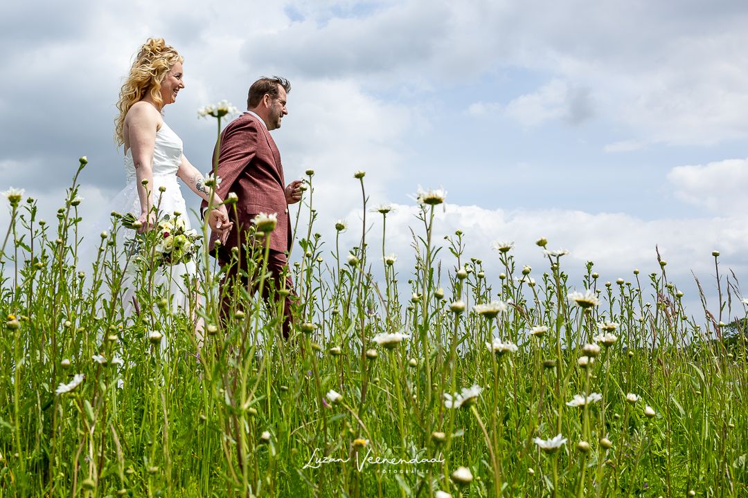 Bruidspaar loopt hand in hand door een bloemenveld tijdens trouwfotoshoot