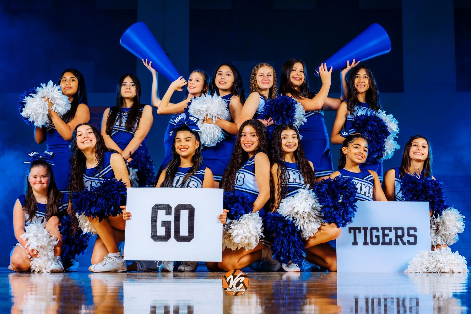 A cheerleading squad in blue uniforms poses with GO TIGERS signs and blue pom-poms for a team photo.