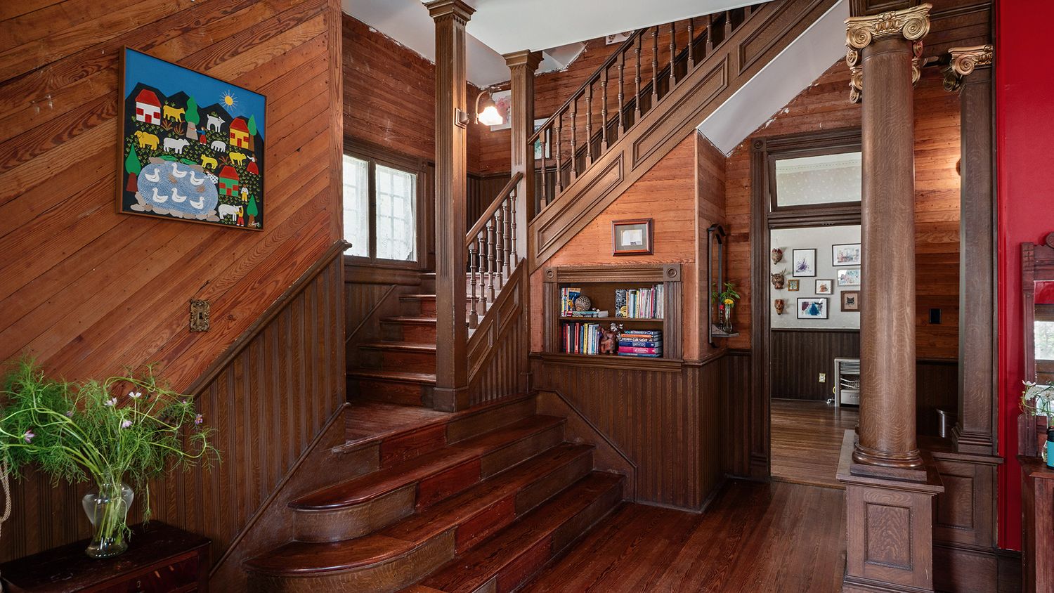 Elegant wooden staircase with ornate carved columns, rich mahogany floors, and colorful wall art in a classic Victorian home.