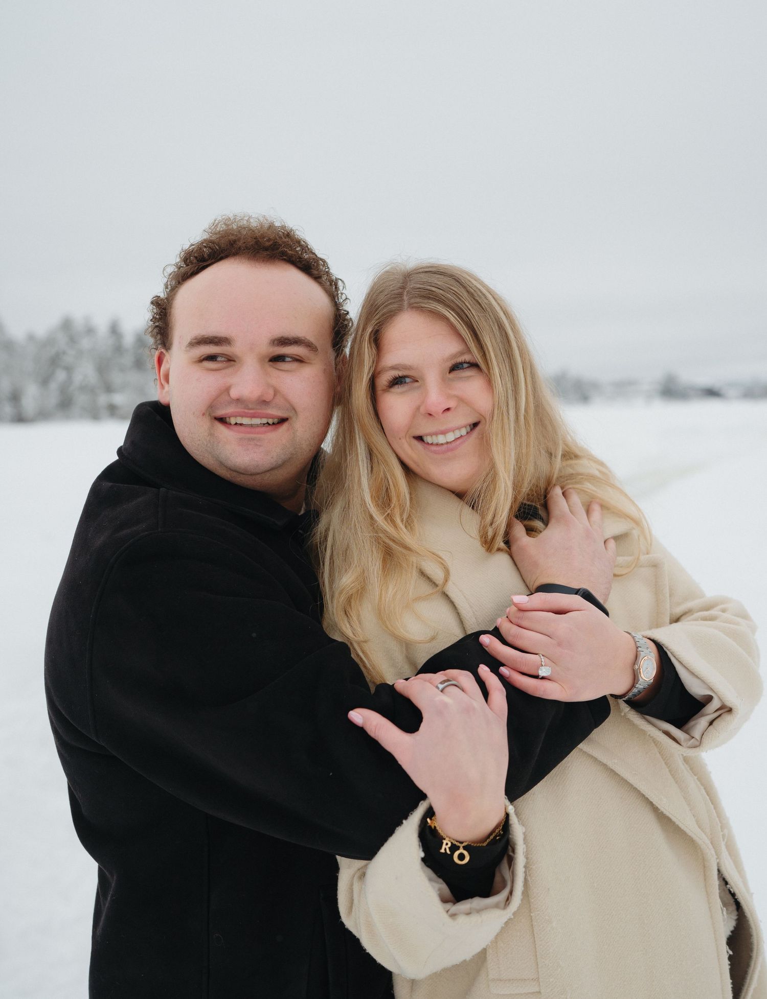 A couple embraces in a romantic winter photoshoot with snow-covered scenery in the background.