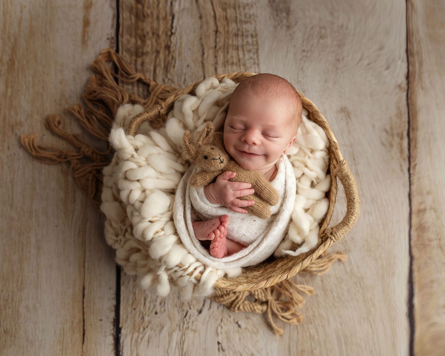 Neutral colours, boho style - image of baby boy curled up in a basket cuddling a teddy, taken in my home studio in Coventry Warwickshire.
