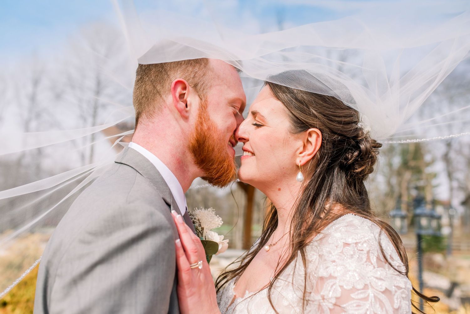 A romantic couple in wedding attire share tender kisses outdoors during a winter photo session.