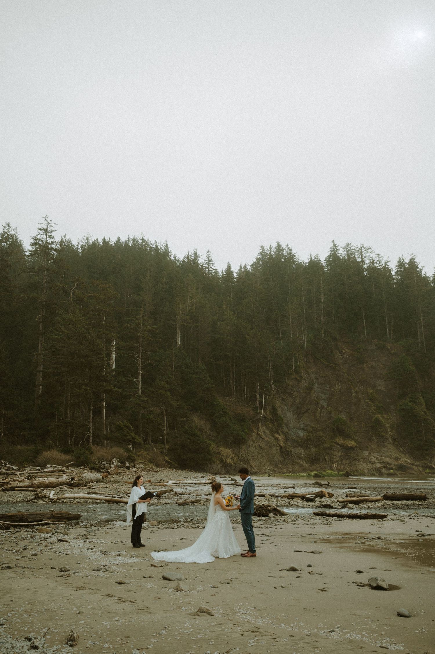 Two figures stand silhouetted against dramatic rocky cliffs during golden hour creating a moody coastal landscape scene.