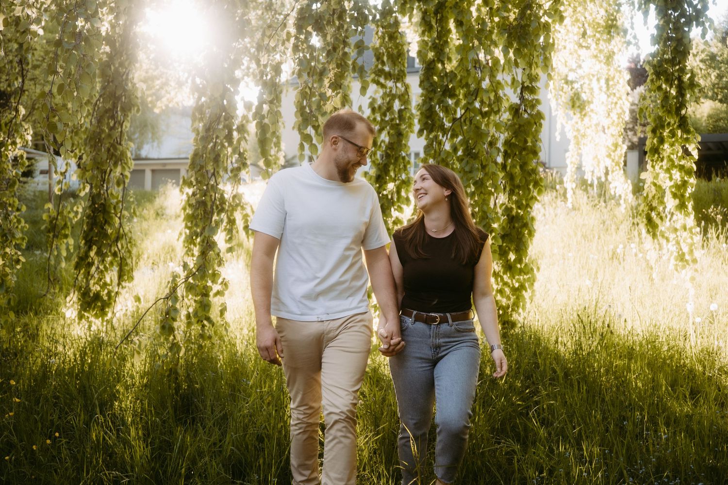 Couple standing together in a classical white columned rotunda gazebo surrounded by lush green trees in a park.