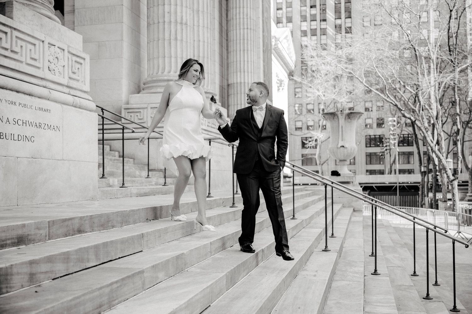 A couple in wedding attire walks down an elegant marble staircase inside a grand neoclassical building.