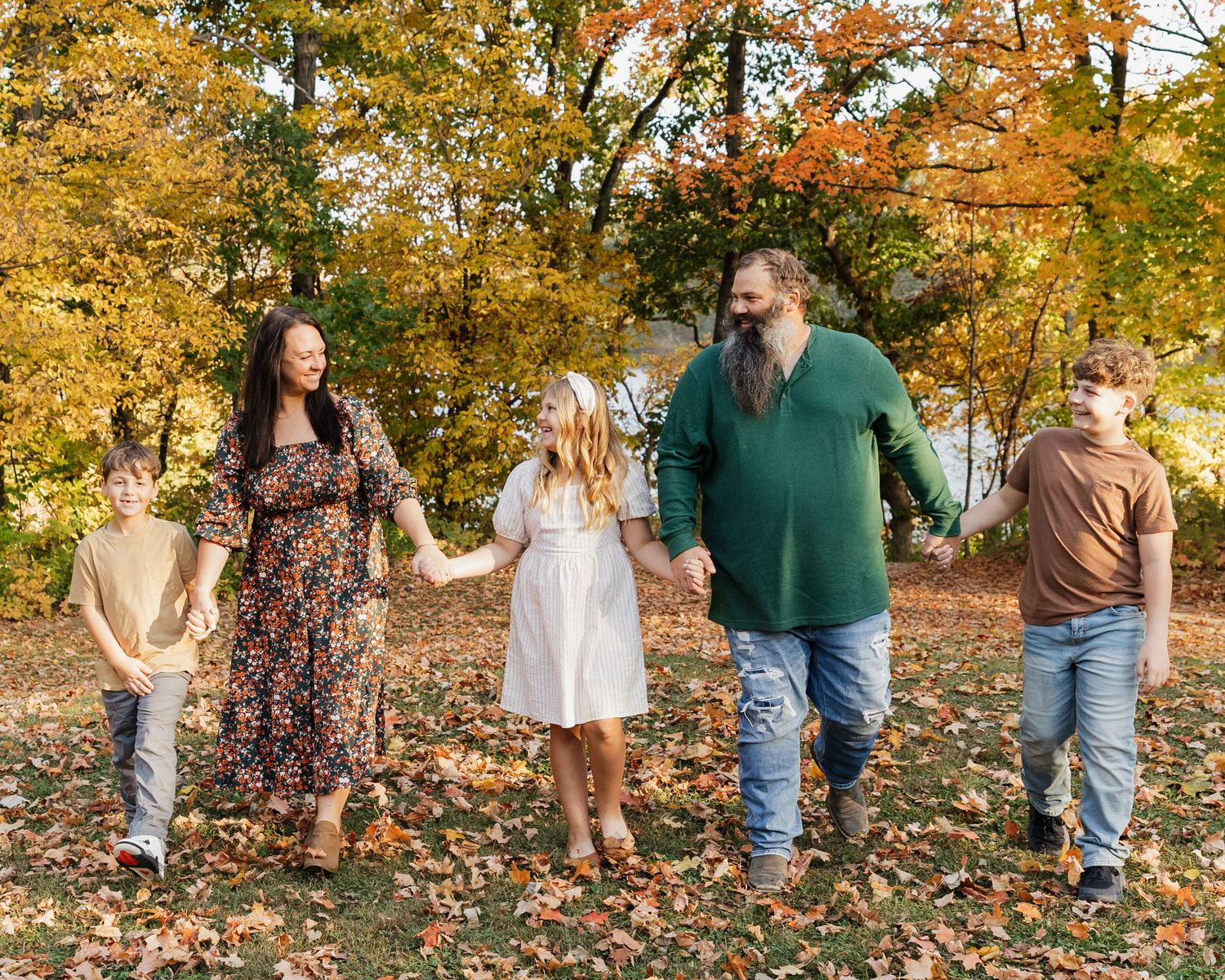 A couple walks through vibrant autumn foliage in a park during a fall photoshoot session.