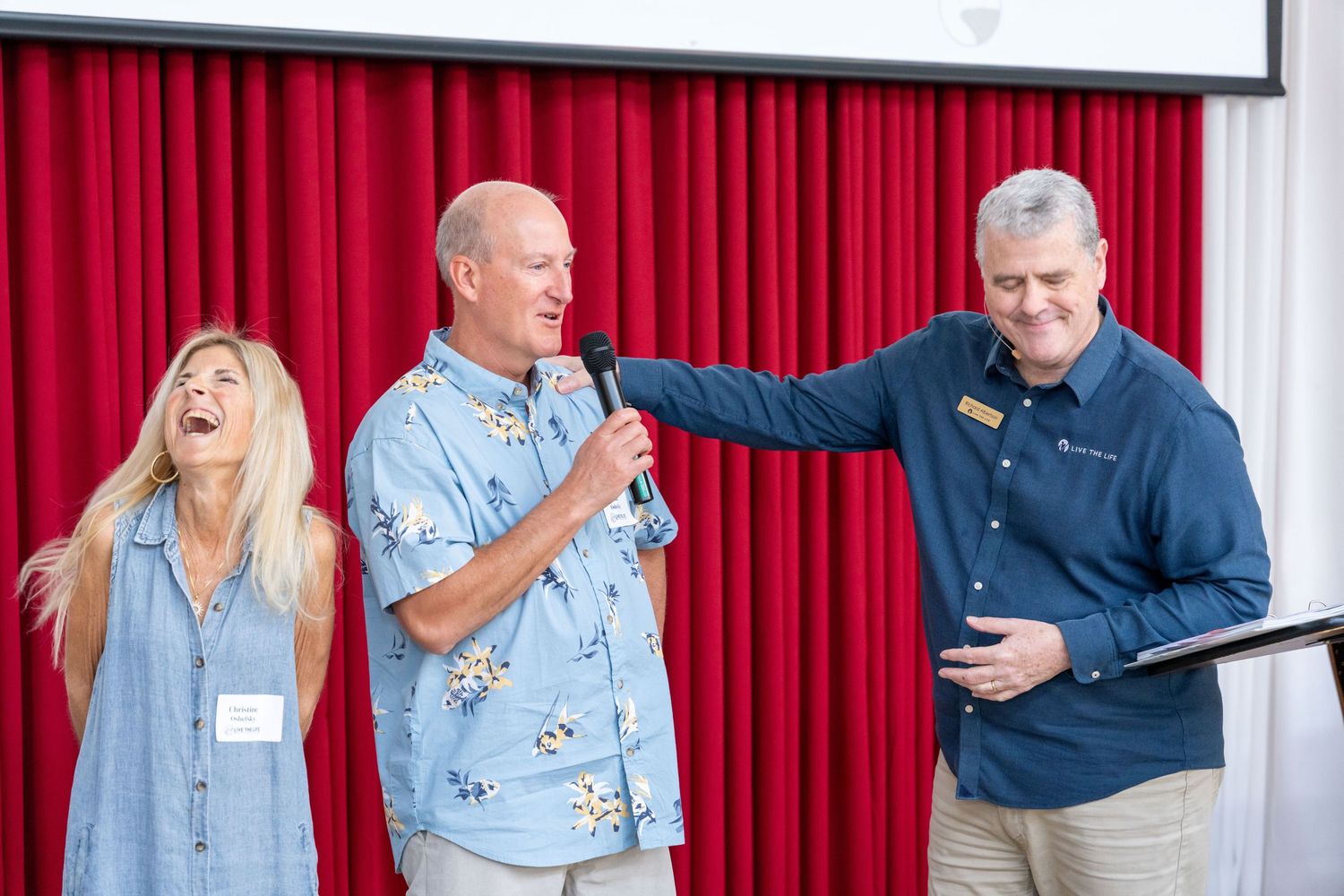 Three people engaged in conversation at a networking event with blue balloon decorations in the background.
