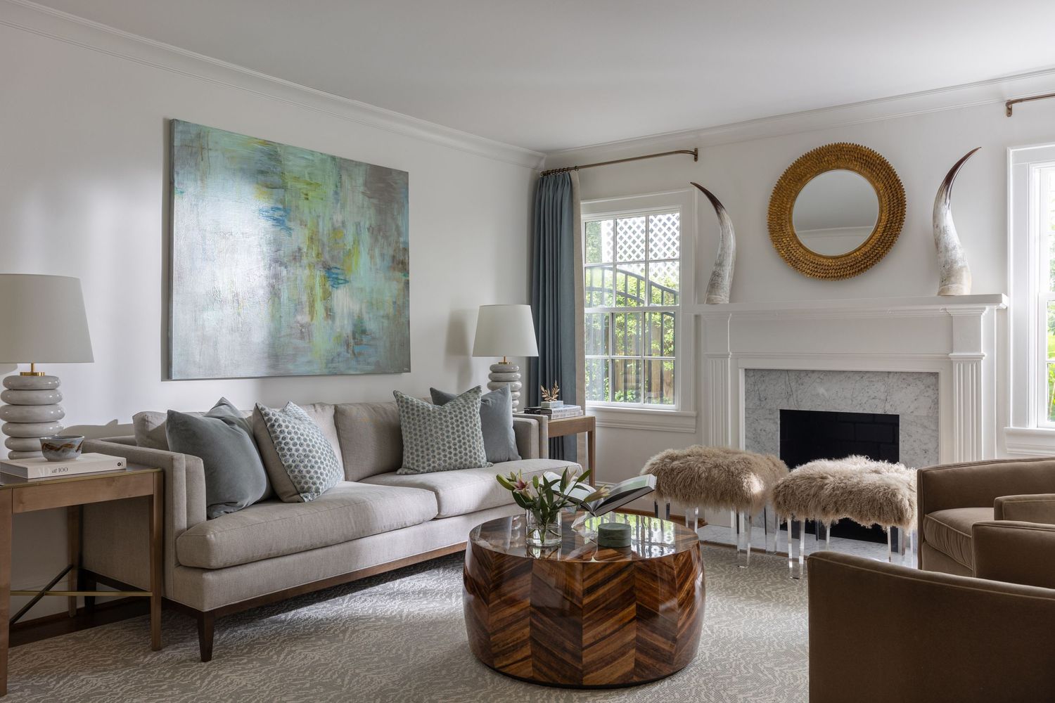 Modern living room with grey sofa, abstract art, round mirror, and natural light from windows.