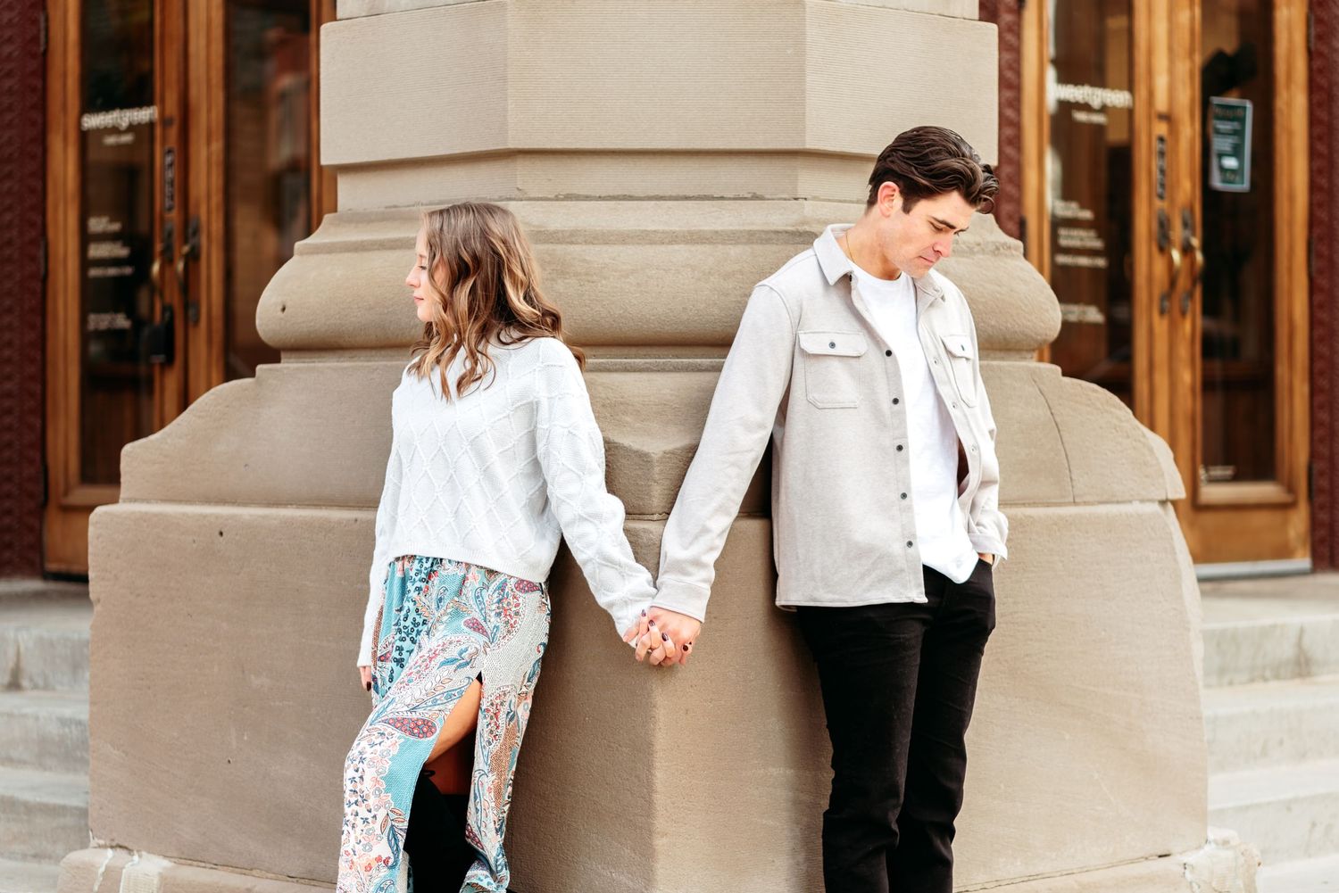 Casual couple holding hands while standing against a stone building exterior.
