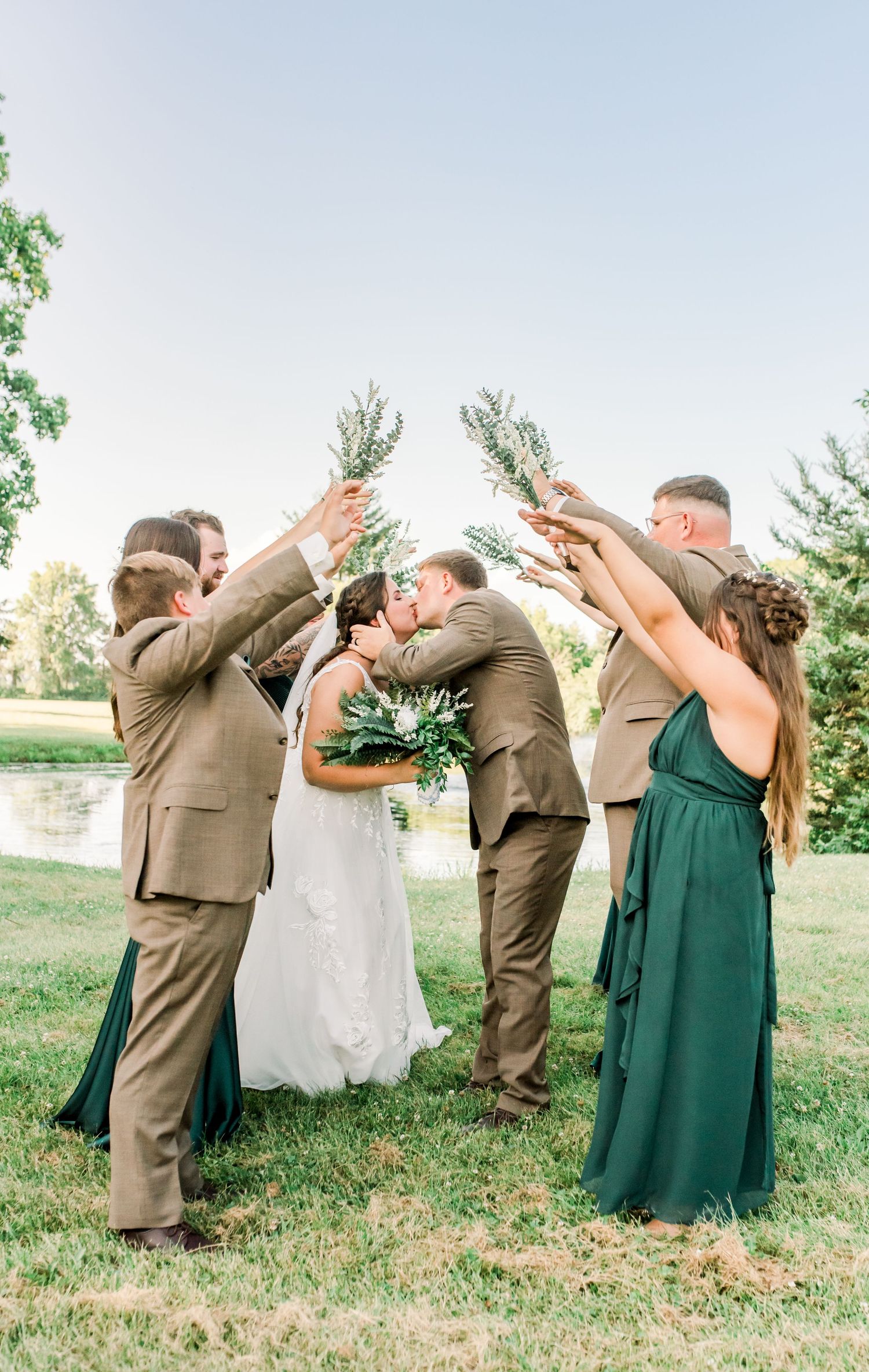 Romantic outdoor wedding moment captured in soft natural light with flowing white veil and greenery bouquet detail.
