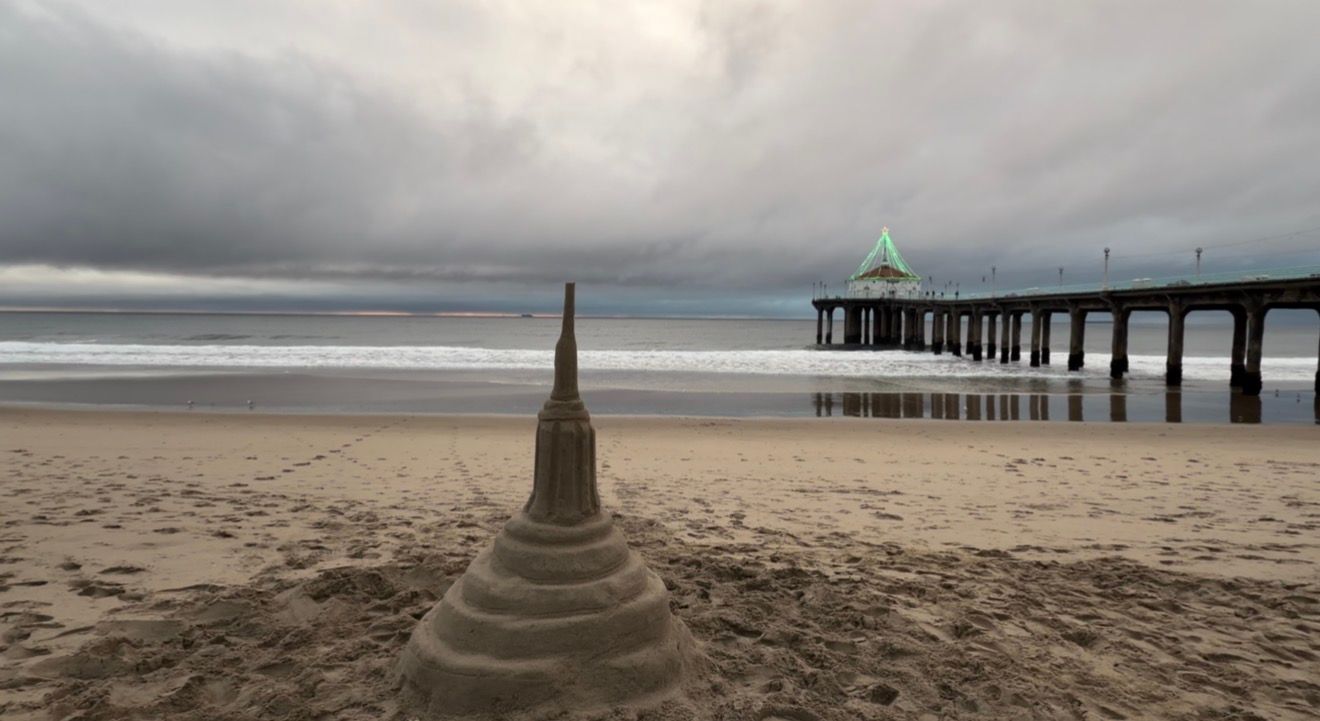 Moody seascape with dramatic clouds over a sandy beach and pier stretching into the ocean at dusk.
