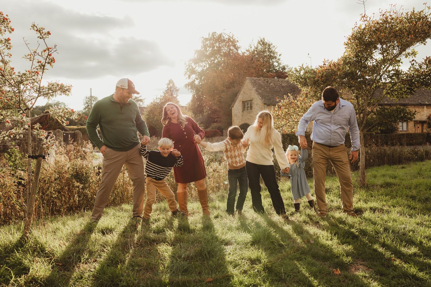A group of people stand together in a grassy field at sunset creating long shadows on the ground.