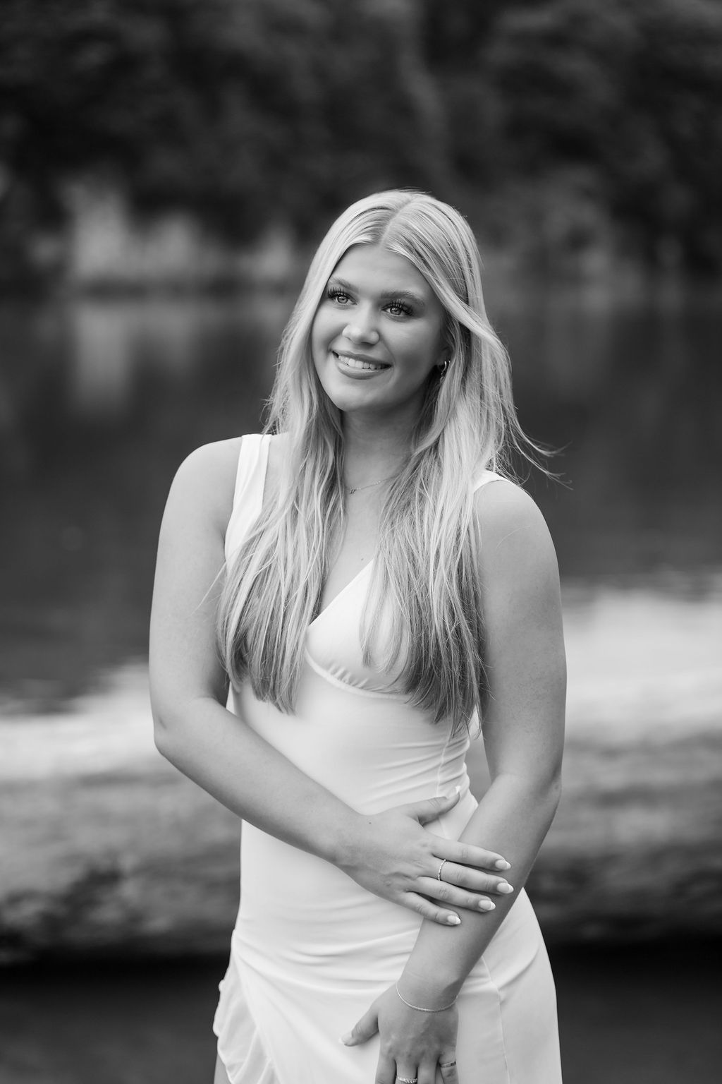 A black and white photo series of a person in a white sleeveless dress posing outdoors by a lake.