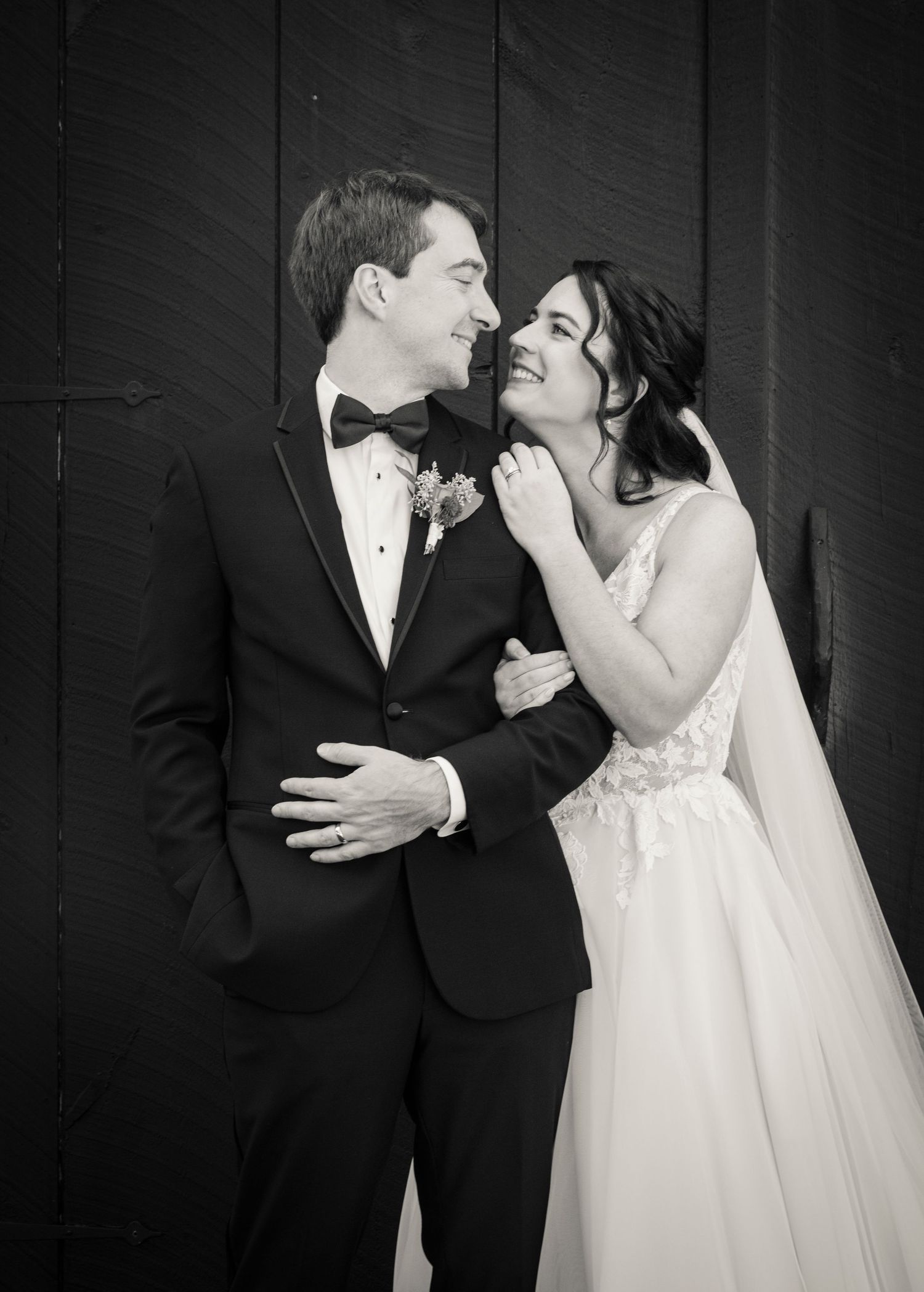 A winter wedding portrait outside a white farmhouse with illuminated windows and a full moon.