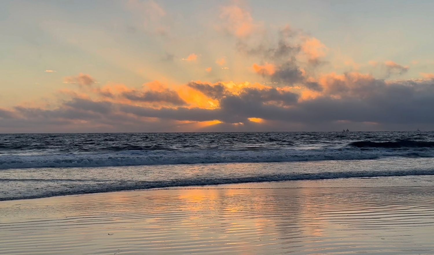 Stunning coastal sunset over the ocean with dramatic orange clouds reflecting on the water's rippling surface.