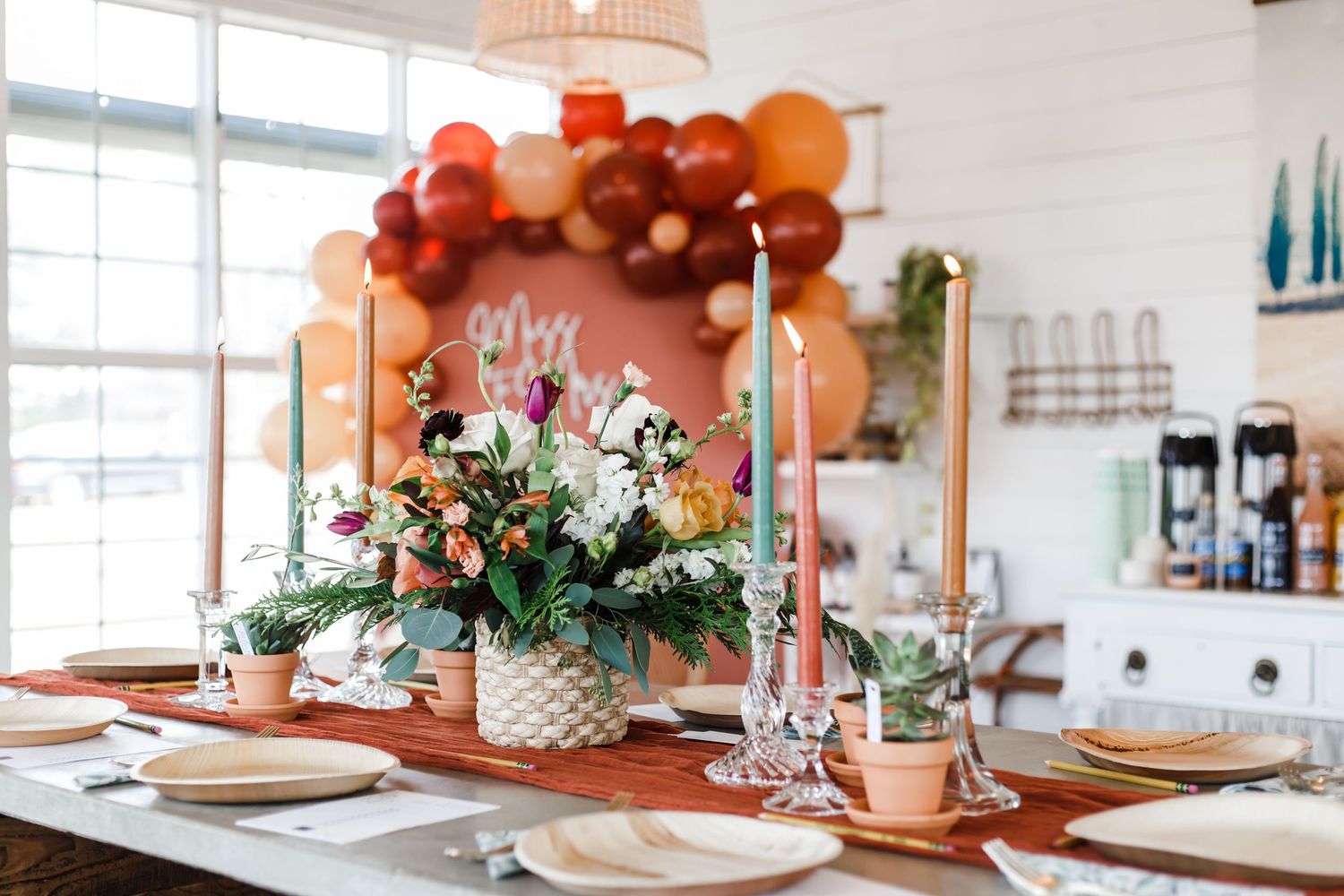 A festive tablescape with orange balloon arch, floral centerpieces, and place settings in a bright dining room.