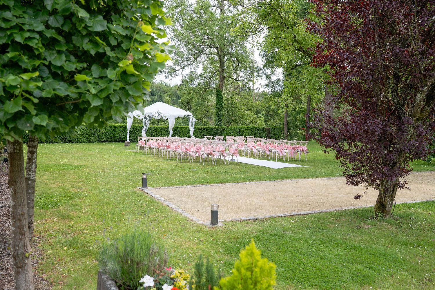 A lush green park landscape with walking paths, decorative plantings, and a small wooden bridge in the distance.