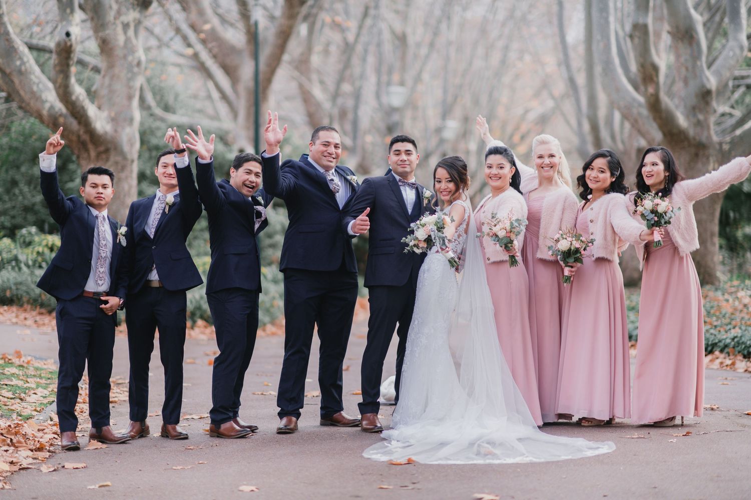 Wedding party poses together on stone steps in formal attire with bridesmaids in pink dresses and groomsmen in navy suits.