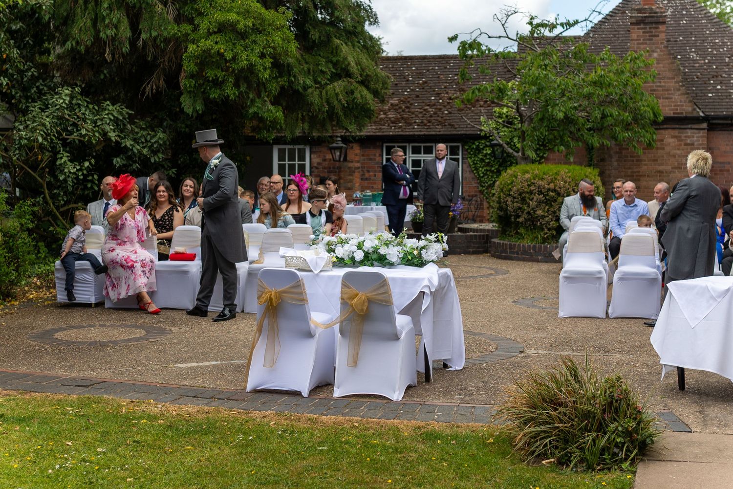 Outdoor wedding reception setup with white chair covers and tables arranged on a rustic brick patio.