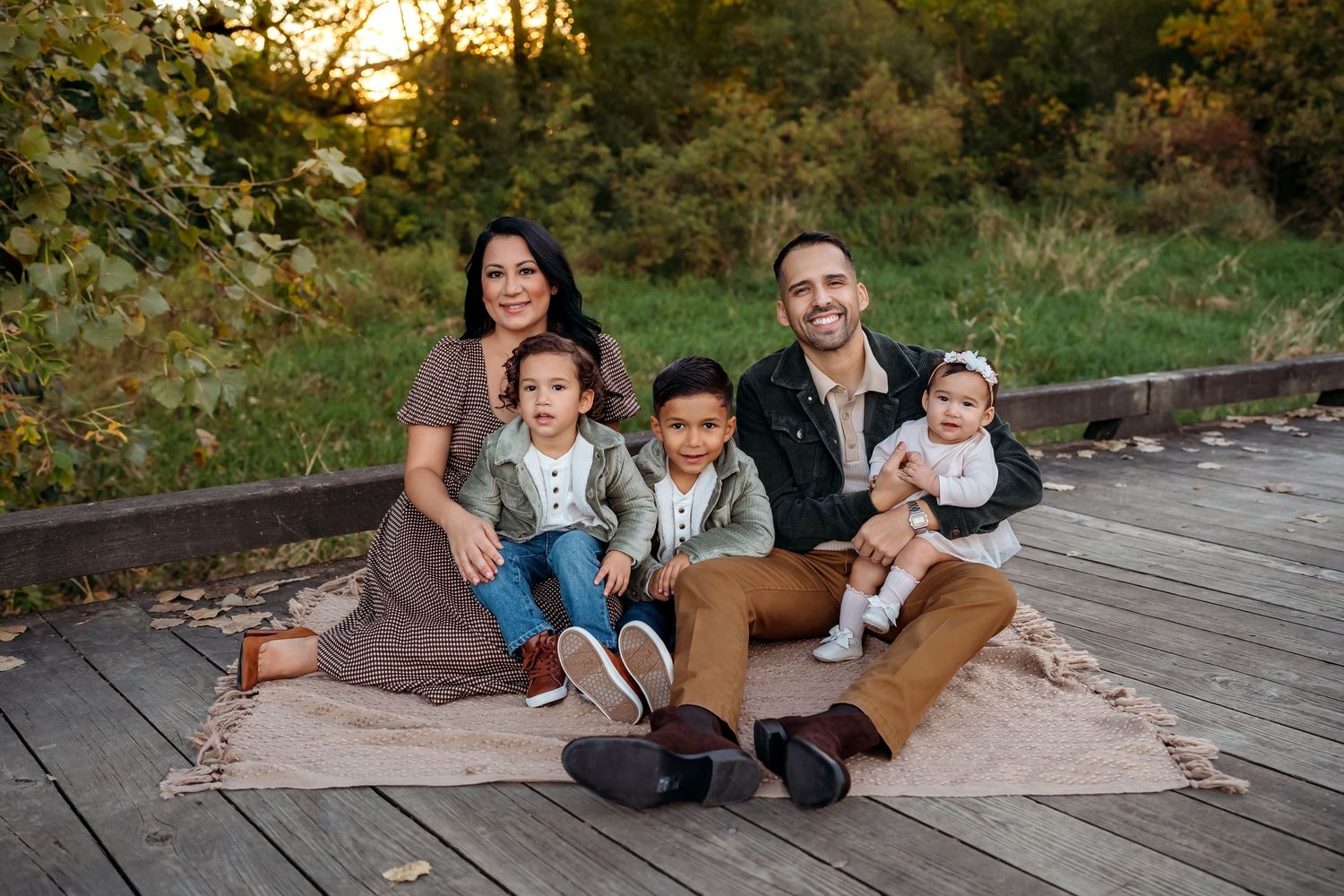 A family walks together on a wooden boardwalk path through autumn foliage in a natural setting.