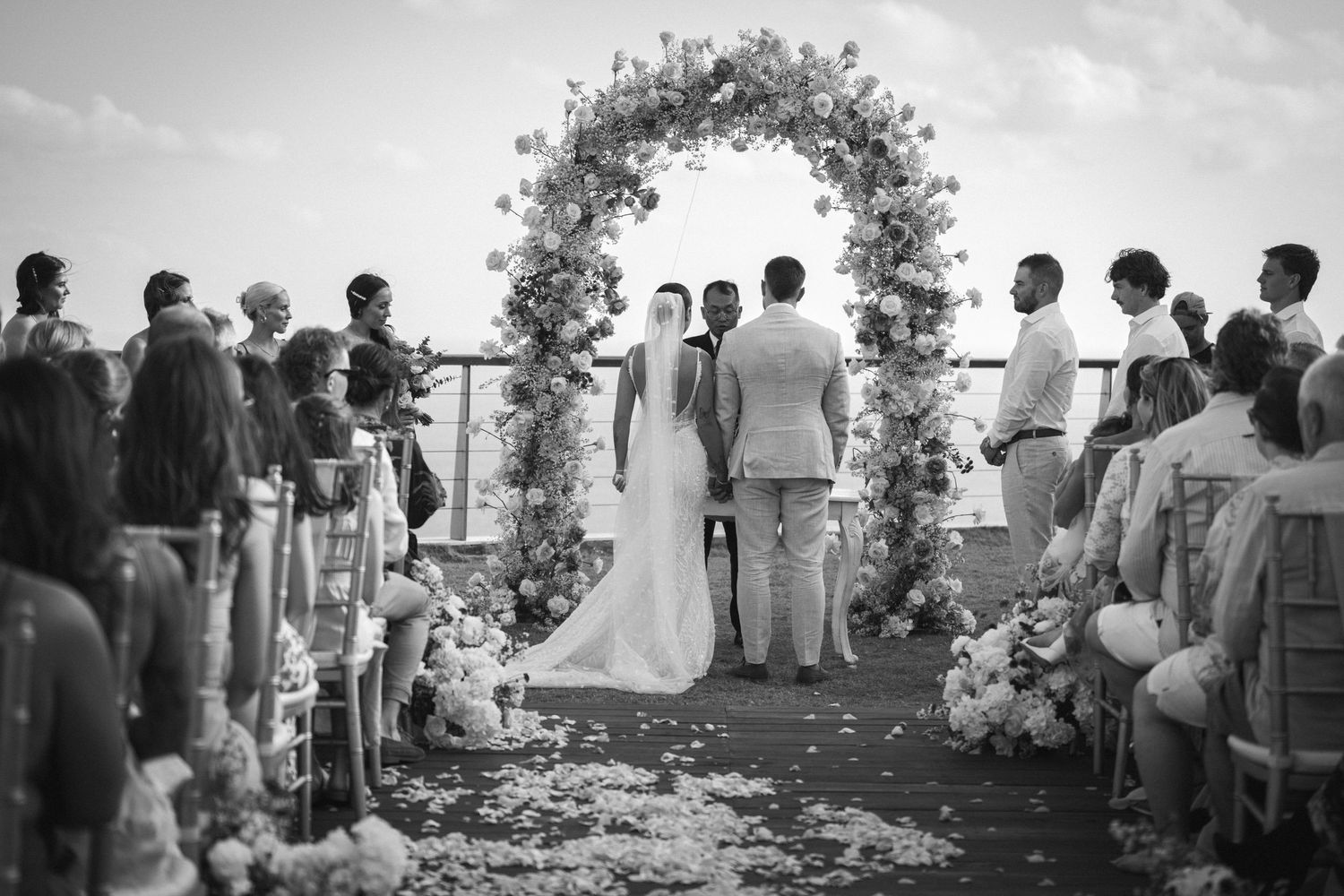 Silhouetted couple sharing a romantic kiss under flowing wedding veil at sunset with dramatic sky in background.