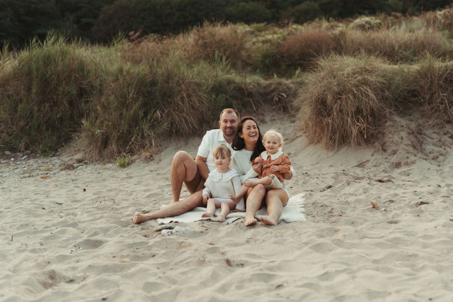 Family sitting together on sand dunes at the beach during sunny evening.