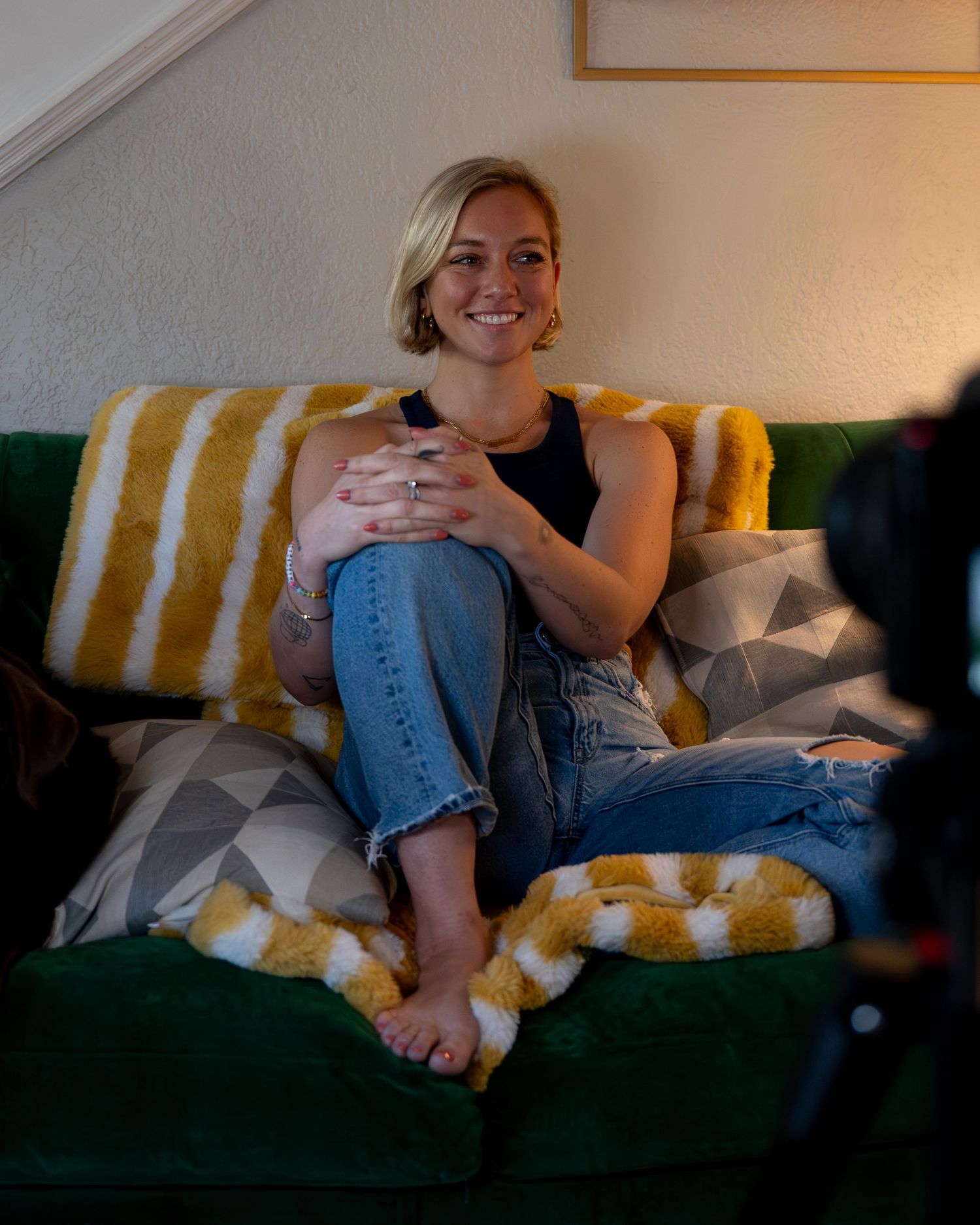Someone relaxes comfortably on a couch with yellow and white striped pillows in a dimly lit room.