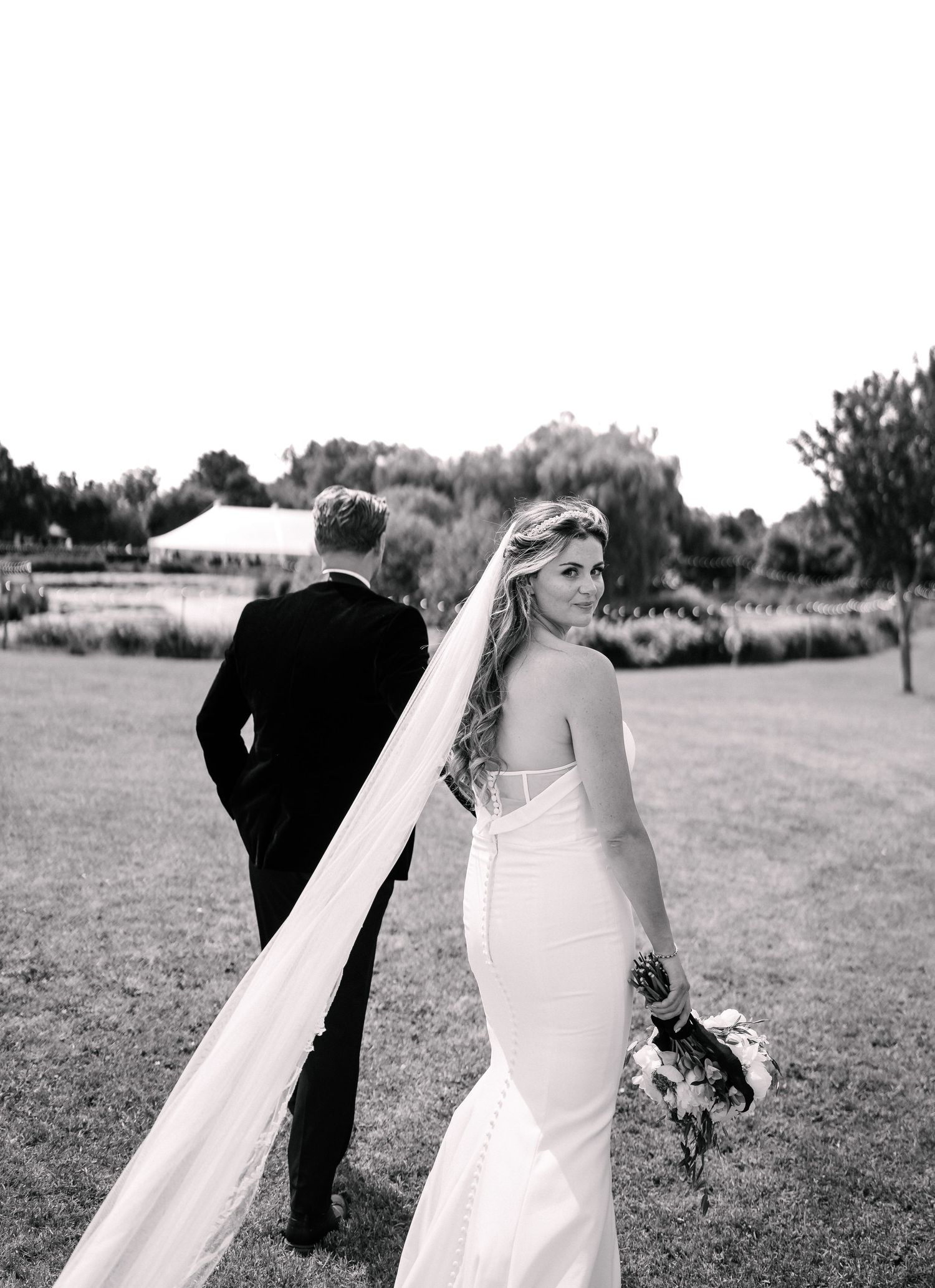 A black and white wedding photo showing a couple in formal attire standing in an outdoor garden setting.