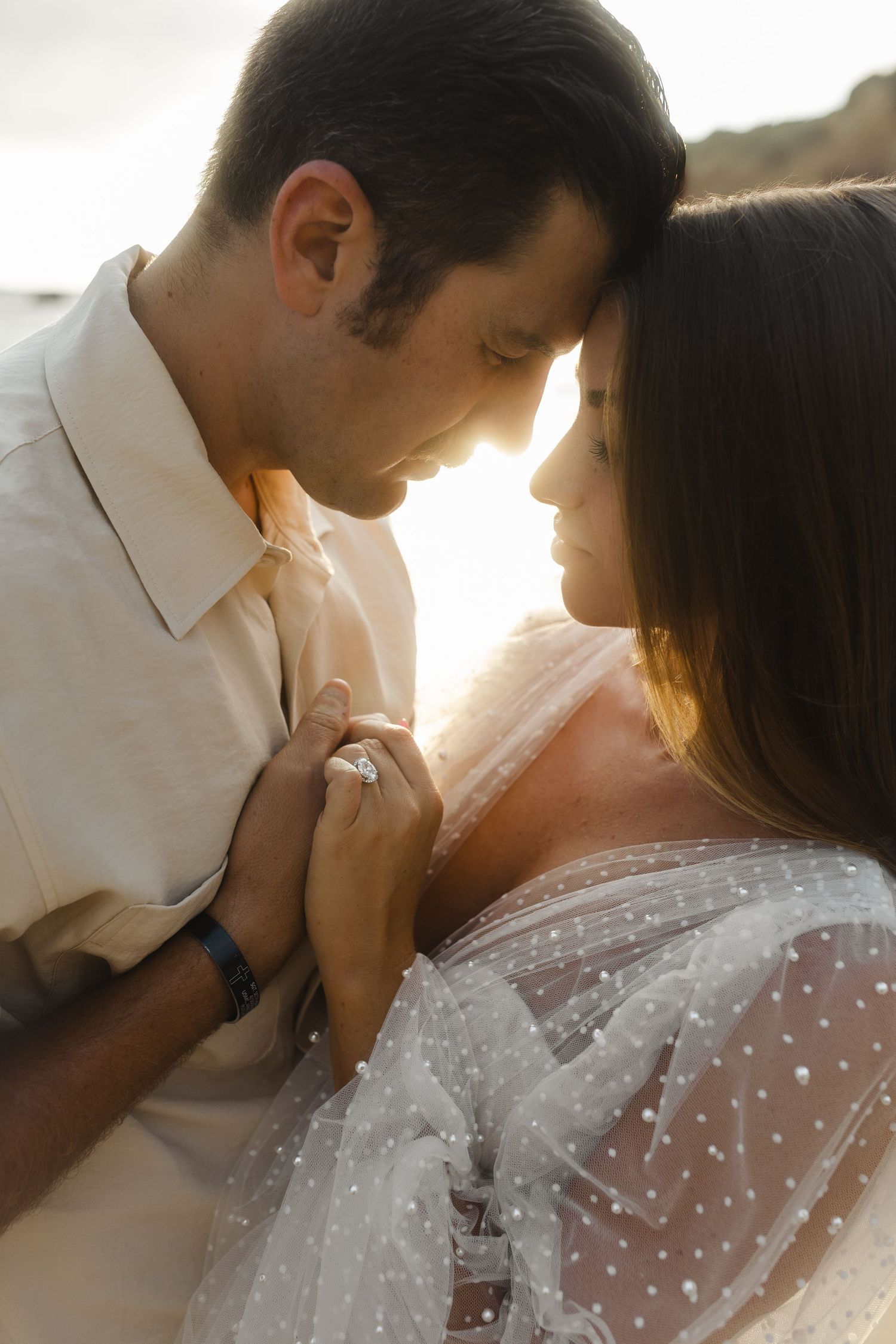 Couple walking on a scenic beach at sunset with flowing white dress in the wind.