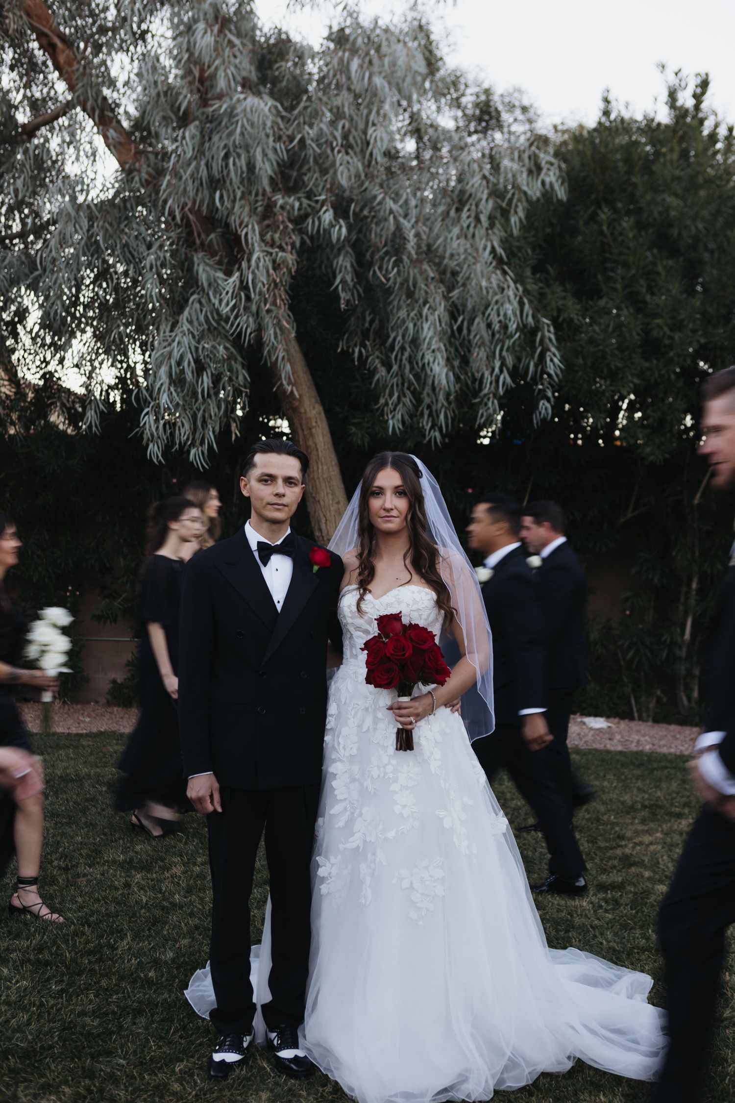 Wedding party gathers outdoors at dusk under wispy trees during an elegant autumn ceremony.