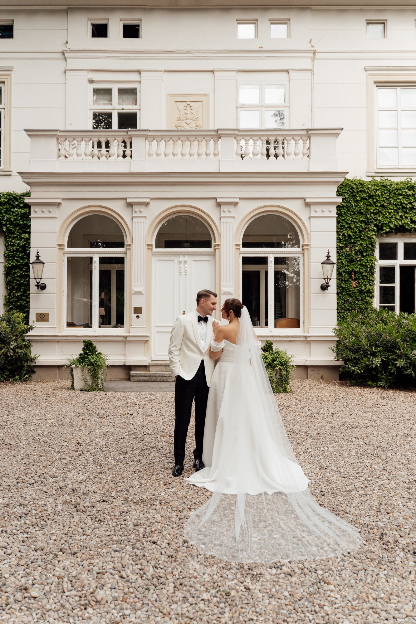 A romantic wedding couple embraces in sunlit garden setting at golden hour.