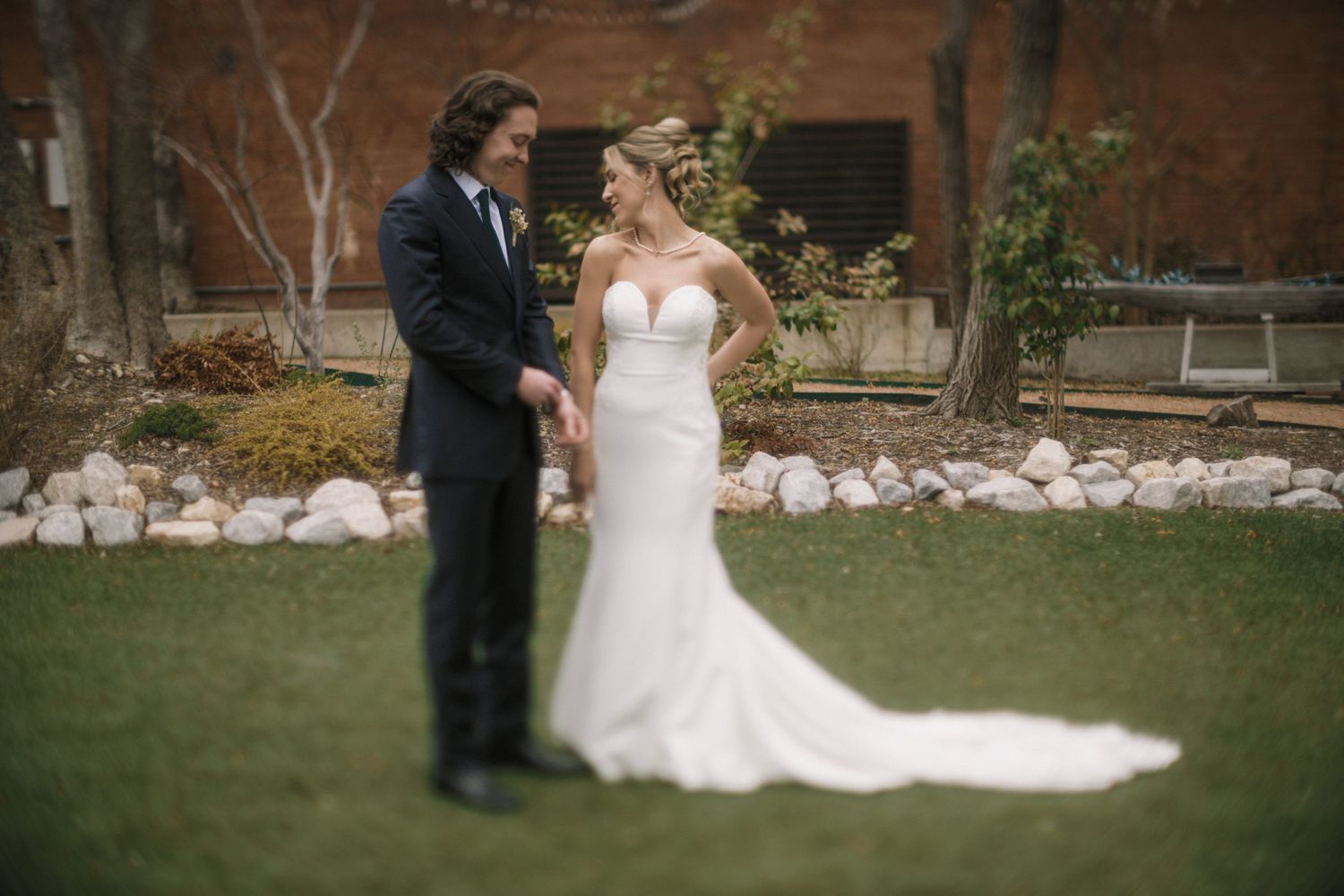 A bride and groom share an intimate moment during their outdoor wedding ceremony in front of a rustic brick wall.