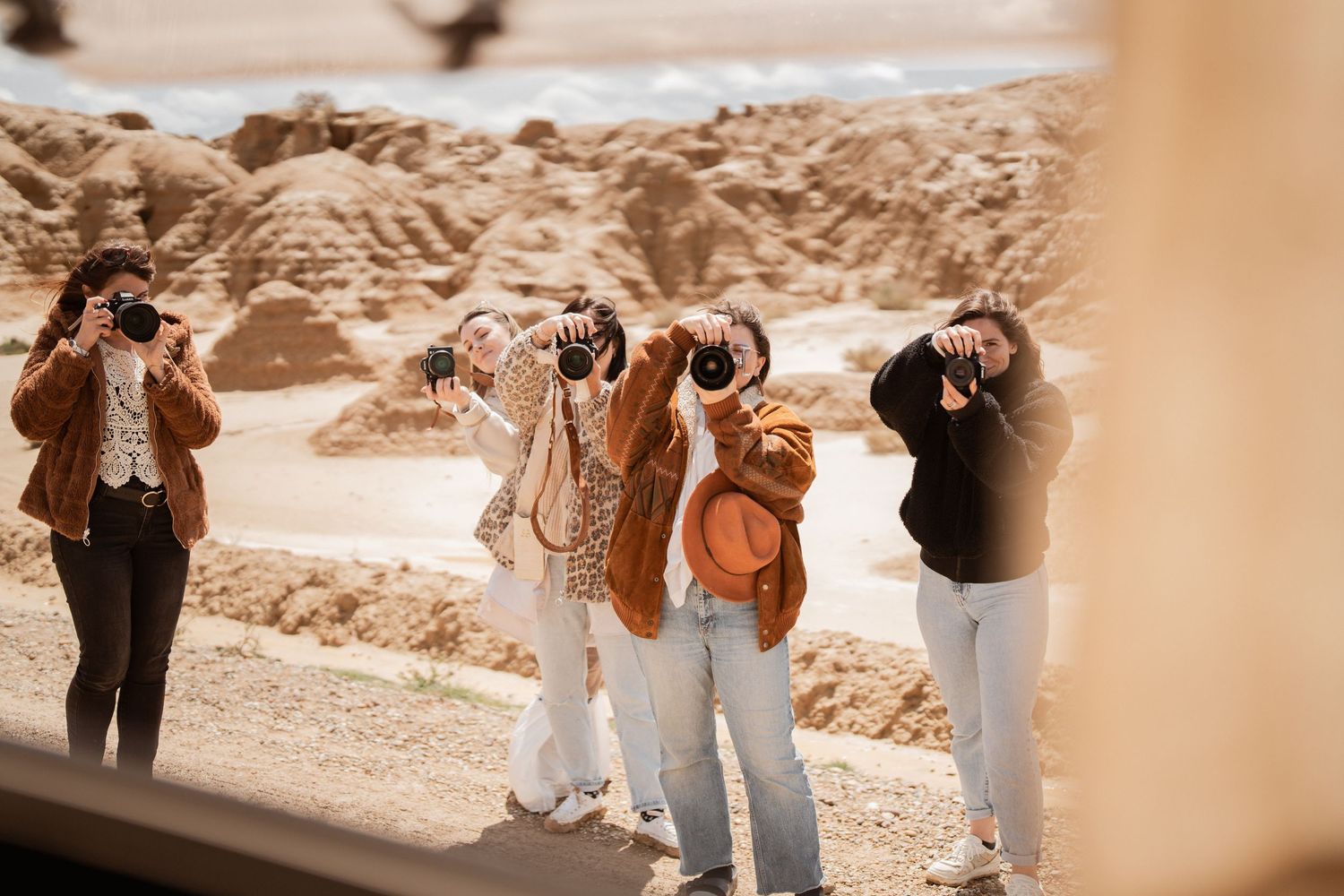 Tourists take photos with cameras in a desert landscape during sunset against rocky terrain.
