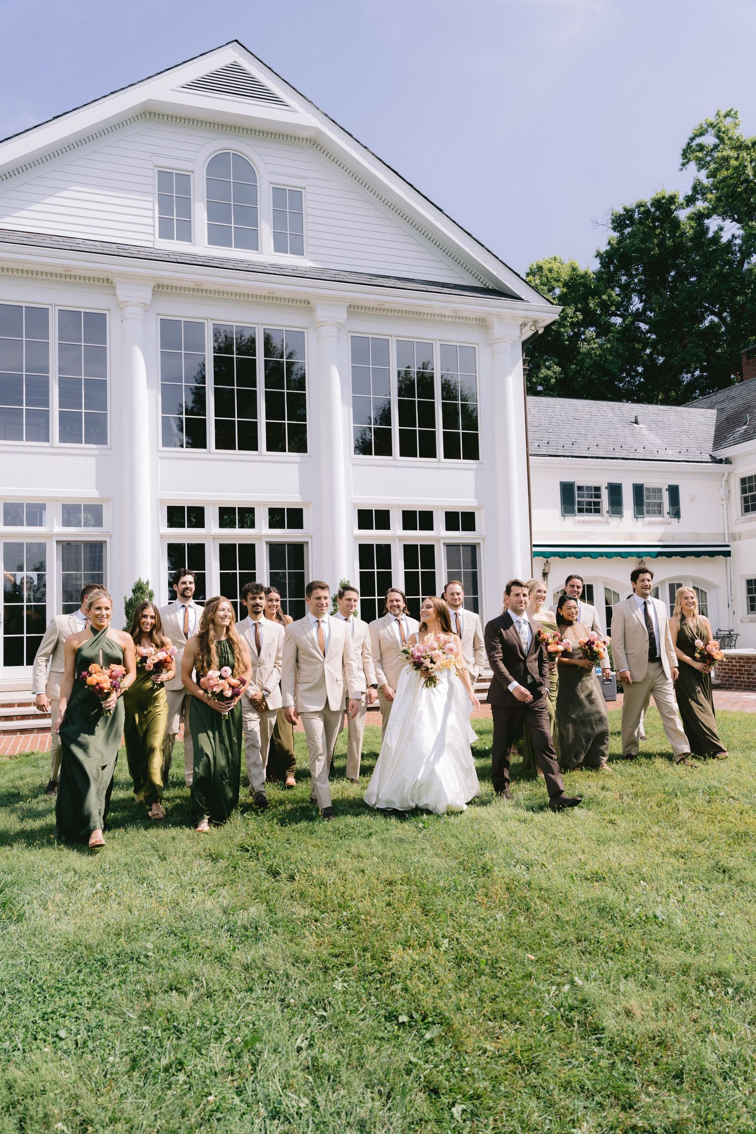 Black and white photo of wedding party gathering on lawn outside elegant mansion venue.