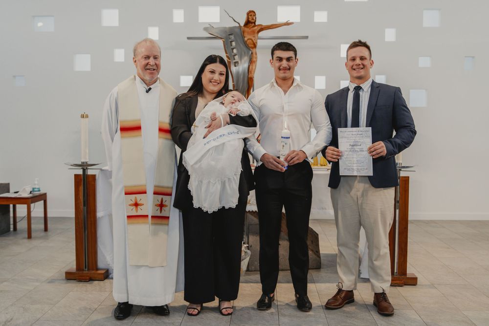 Family gathered for a baby baptism ceremony in a church, with a priest in vestments and guests holding an infant.