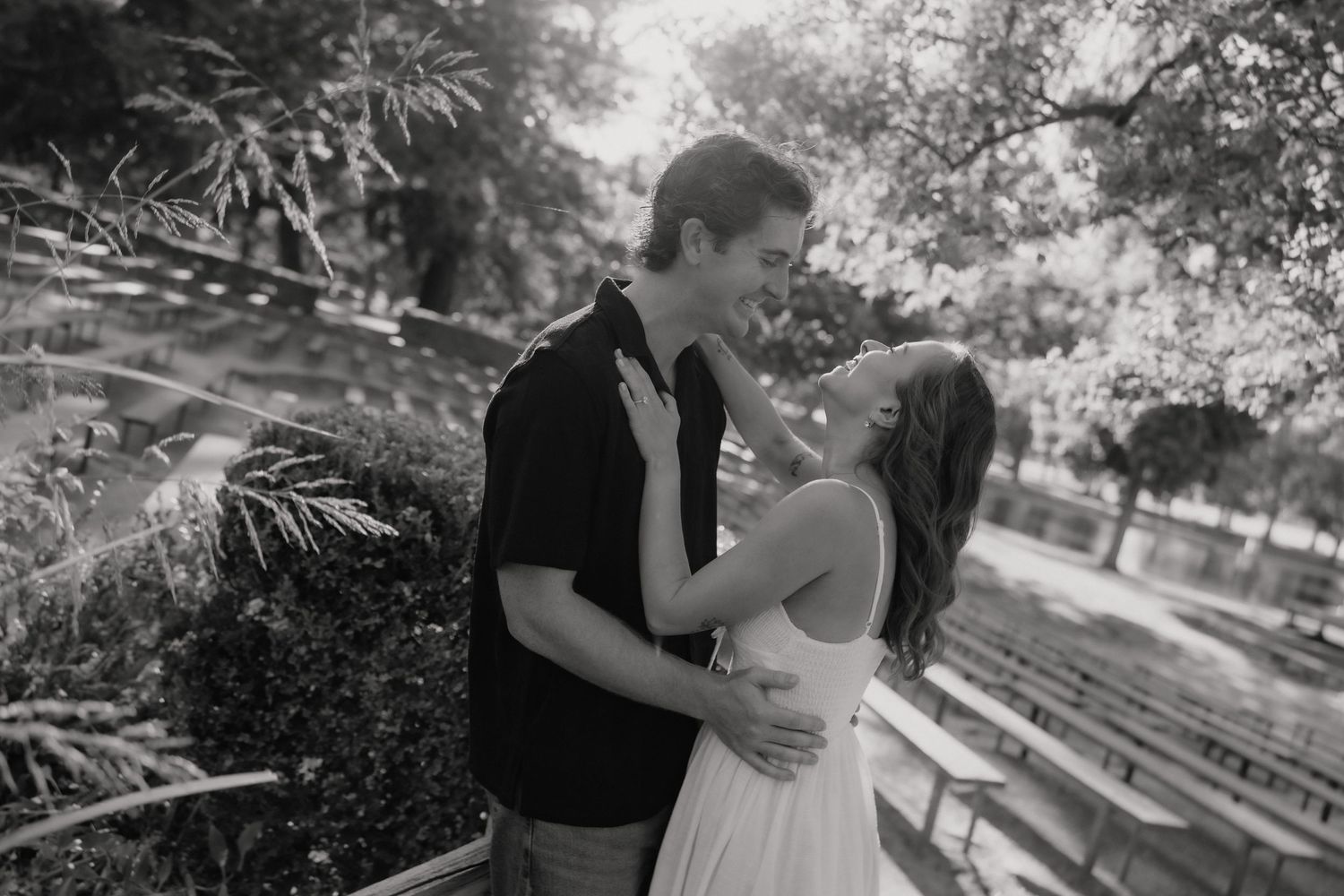 Black and white photo of bride and groom sharing an intimate moment under flowing wedding veil in outdoor field.