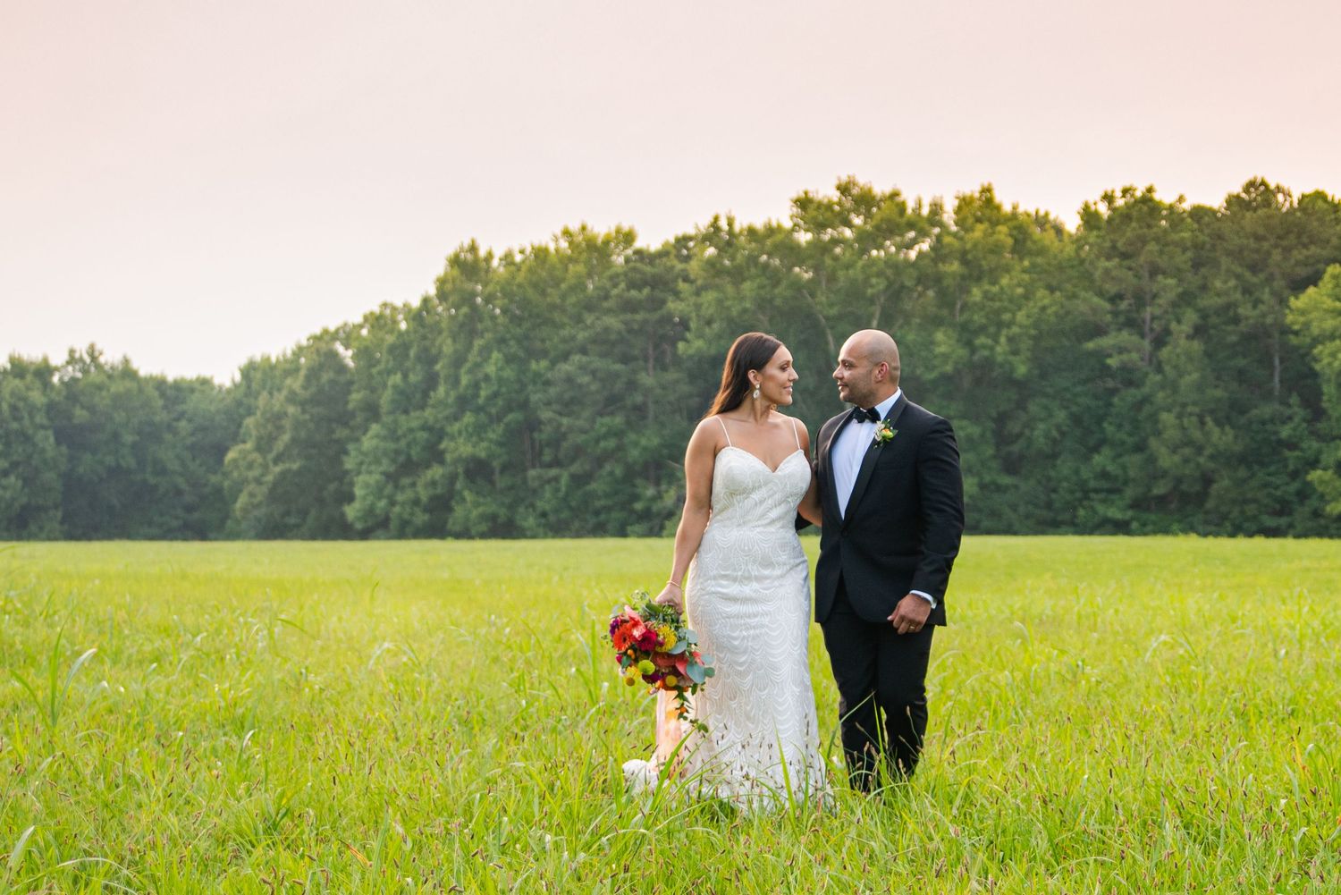 Newlyweds standing together in sunny meadow during golden hour.