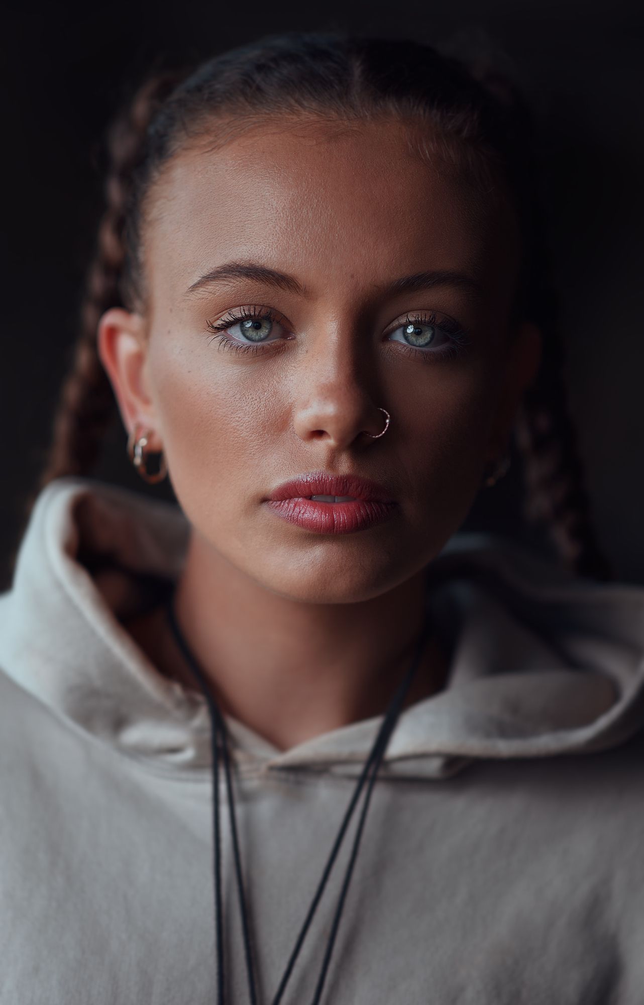 Moody portrait showing pierced nose, braided hair, and a light hoodie.