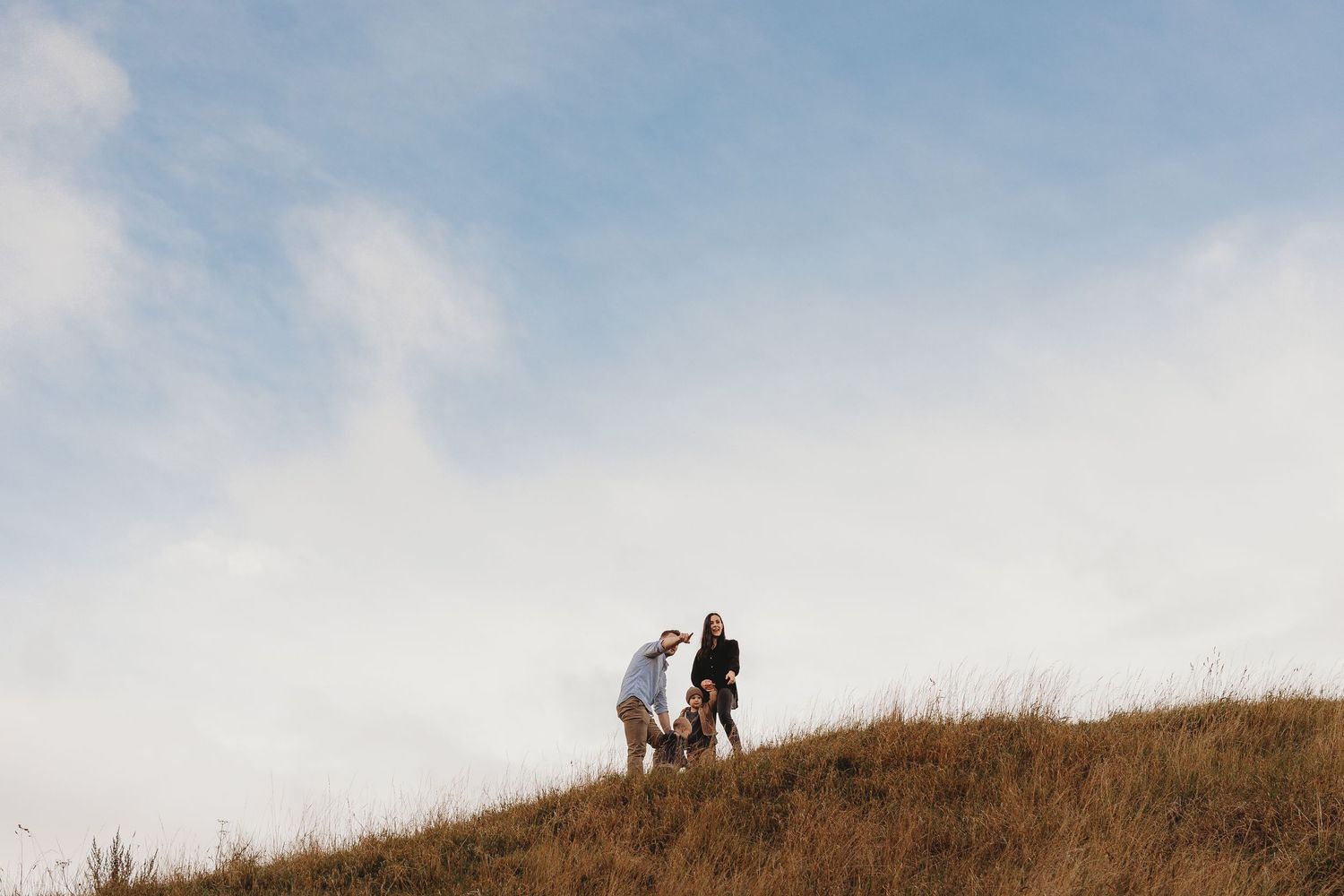 Two hikers walk along a grassy ridgeline trail against a cloudy sky during an autumn day.