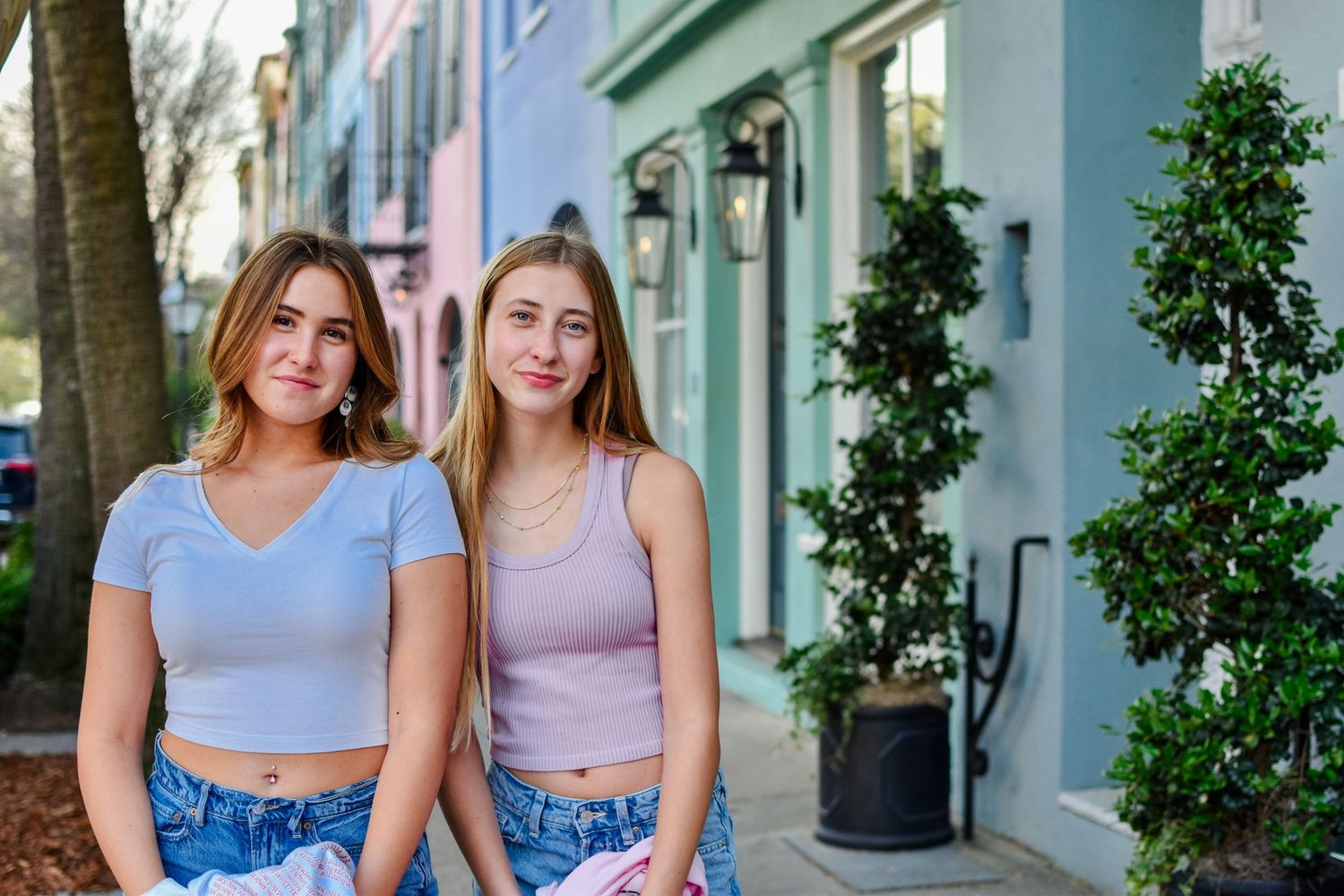 Two friends posing casually in front of colorful buildings on a city street.