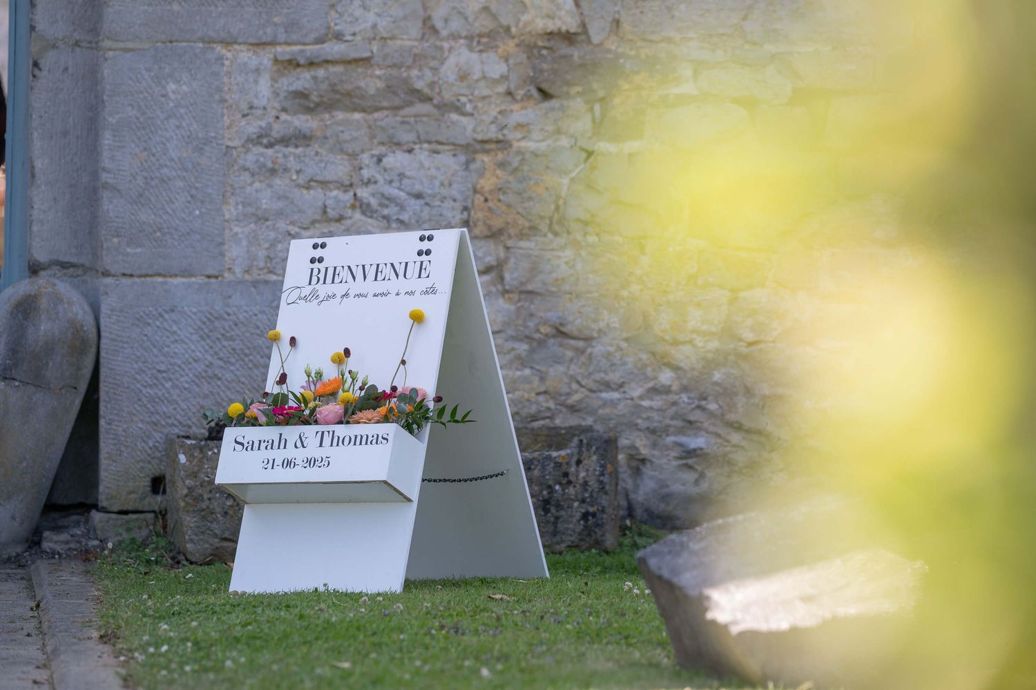 A row of small promotional signs standing in grass against a weathered stone wall with yellow blurred elements.