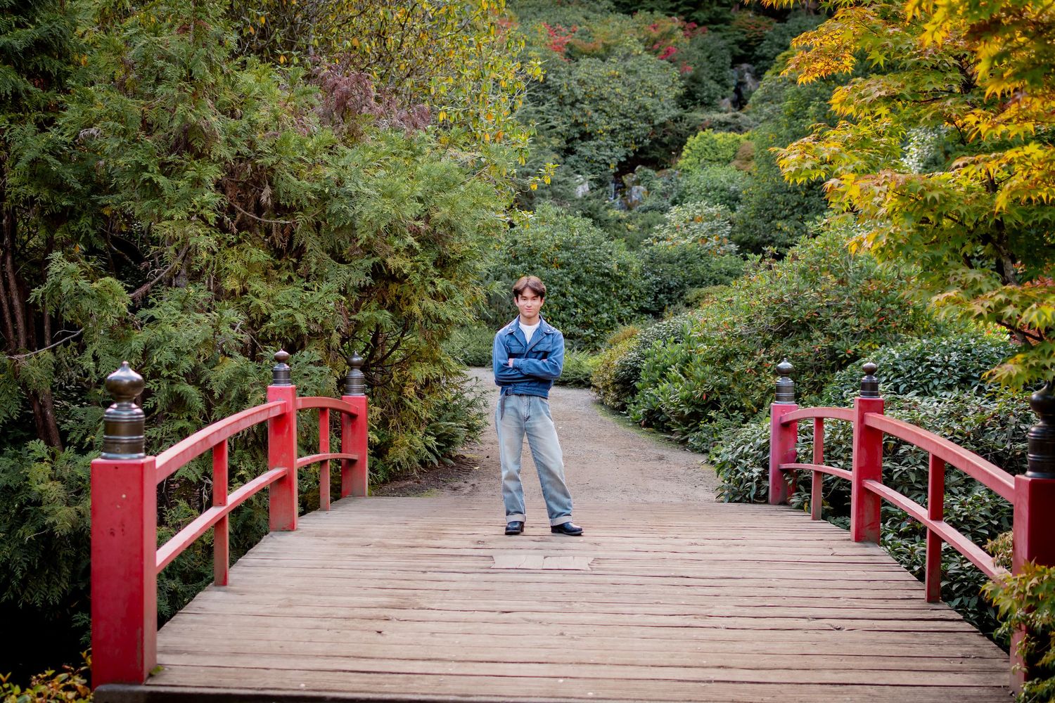 High school senior standing confidently on red bridge surrounded by greenery at Kubota Garden in Seattle