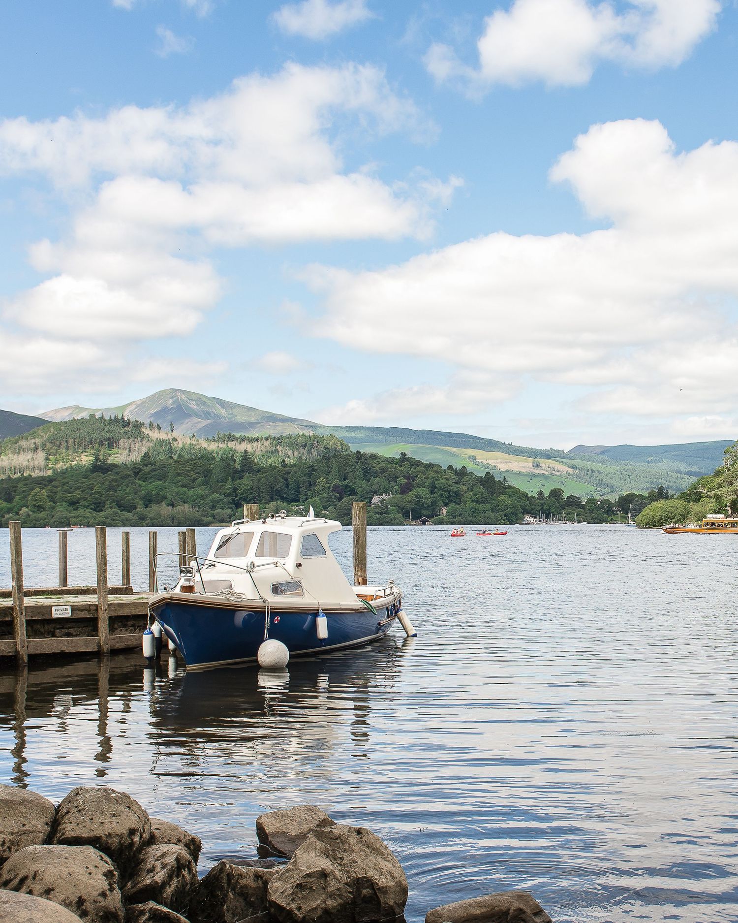 Boats docked at a peaceful lake pier with mountains and blue skies in the background.