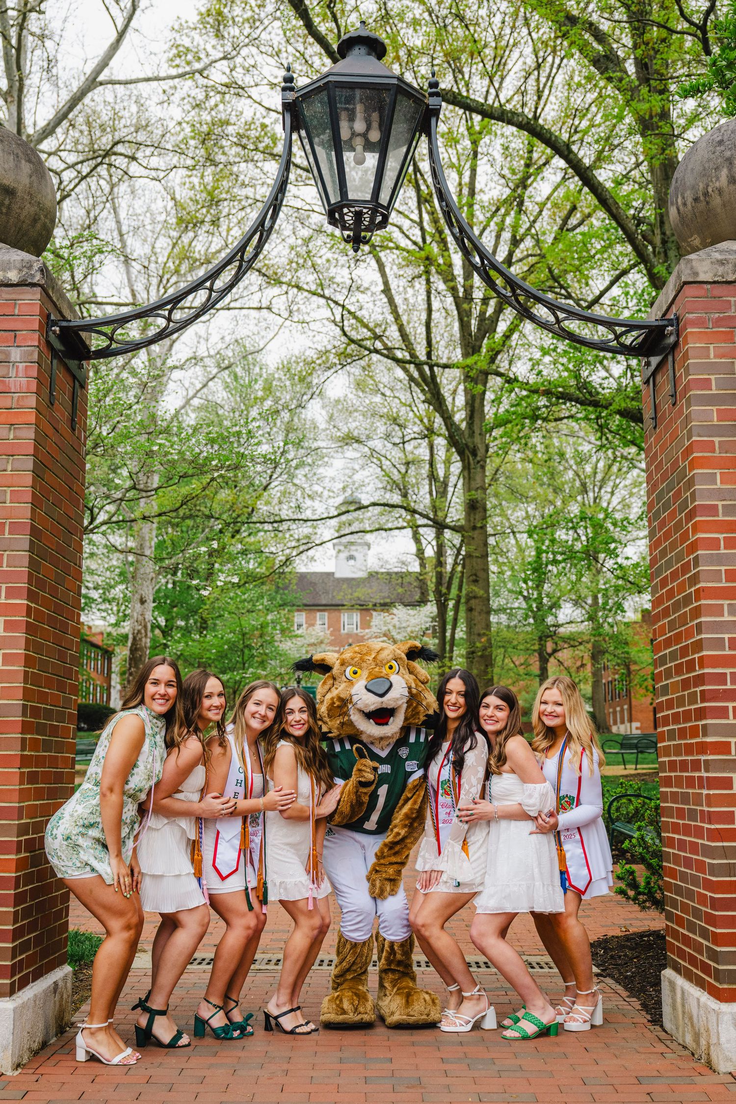 Group in white outfits sitting on brick steps with decorative lanterns and greenery in background.