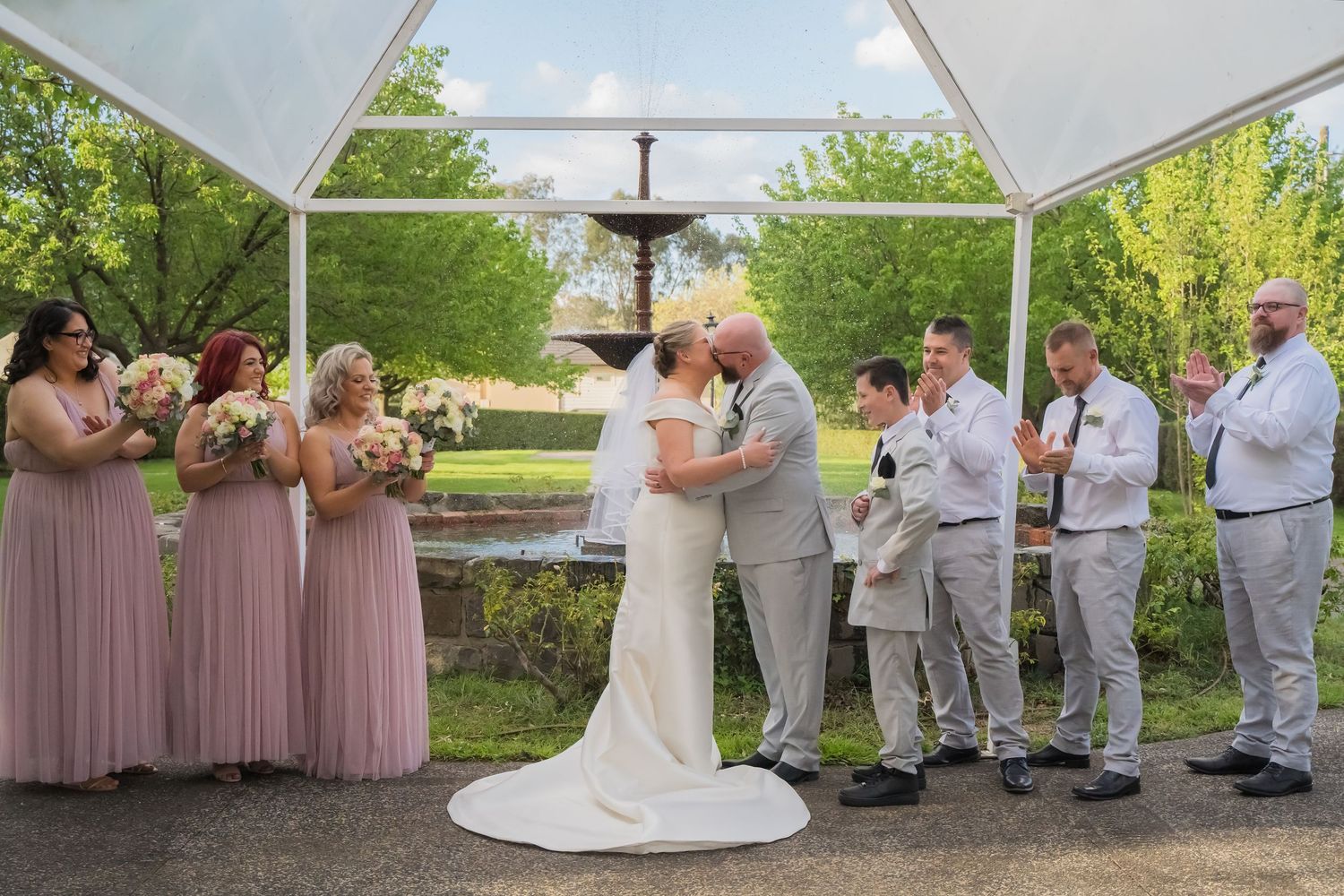 Wedding ceremony takes place under a white tent canopy with guests seated on white chairs.