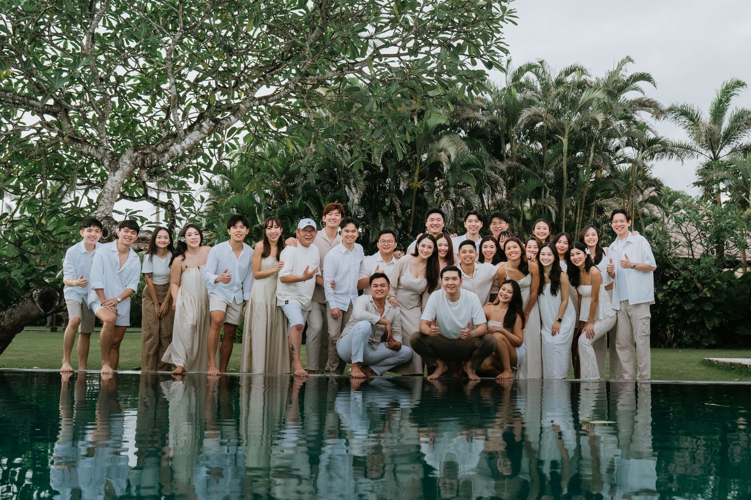 Group photo of people dressed in coordinating light colors gathered outdoors near palm trees.